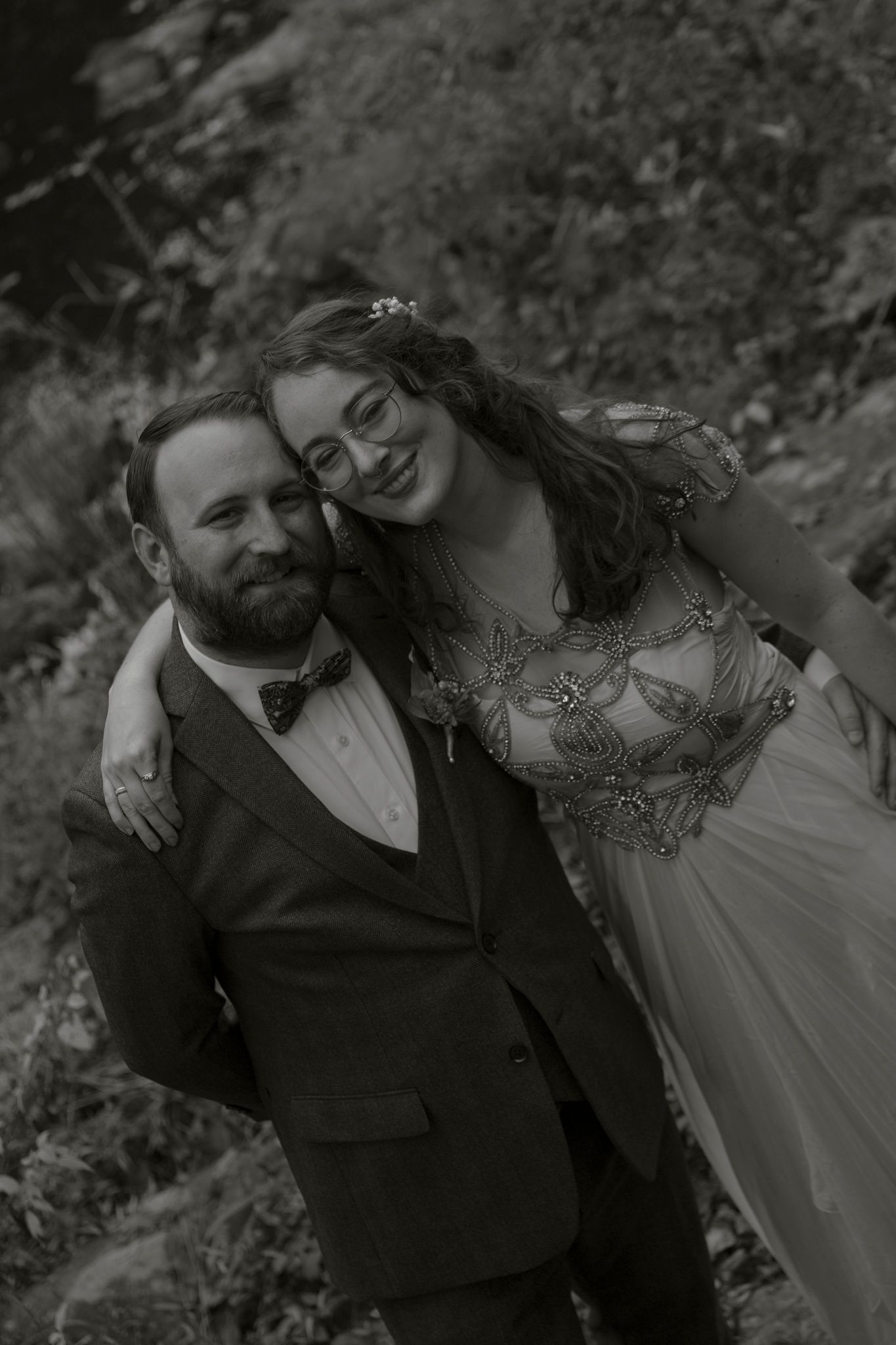 Black and white wedding portrait showing a couple embracing outdoors in formal attire with an ethereal, romantic mood.