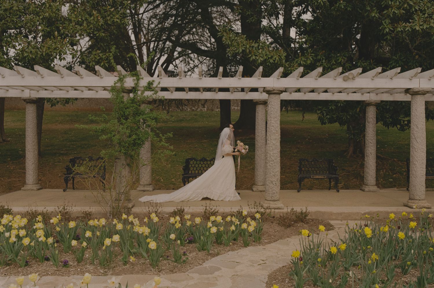 A scenic garden pathway with blooming tulips leads to a white pergola structure in a tranquil outdoor setting.