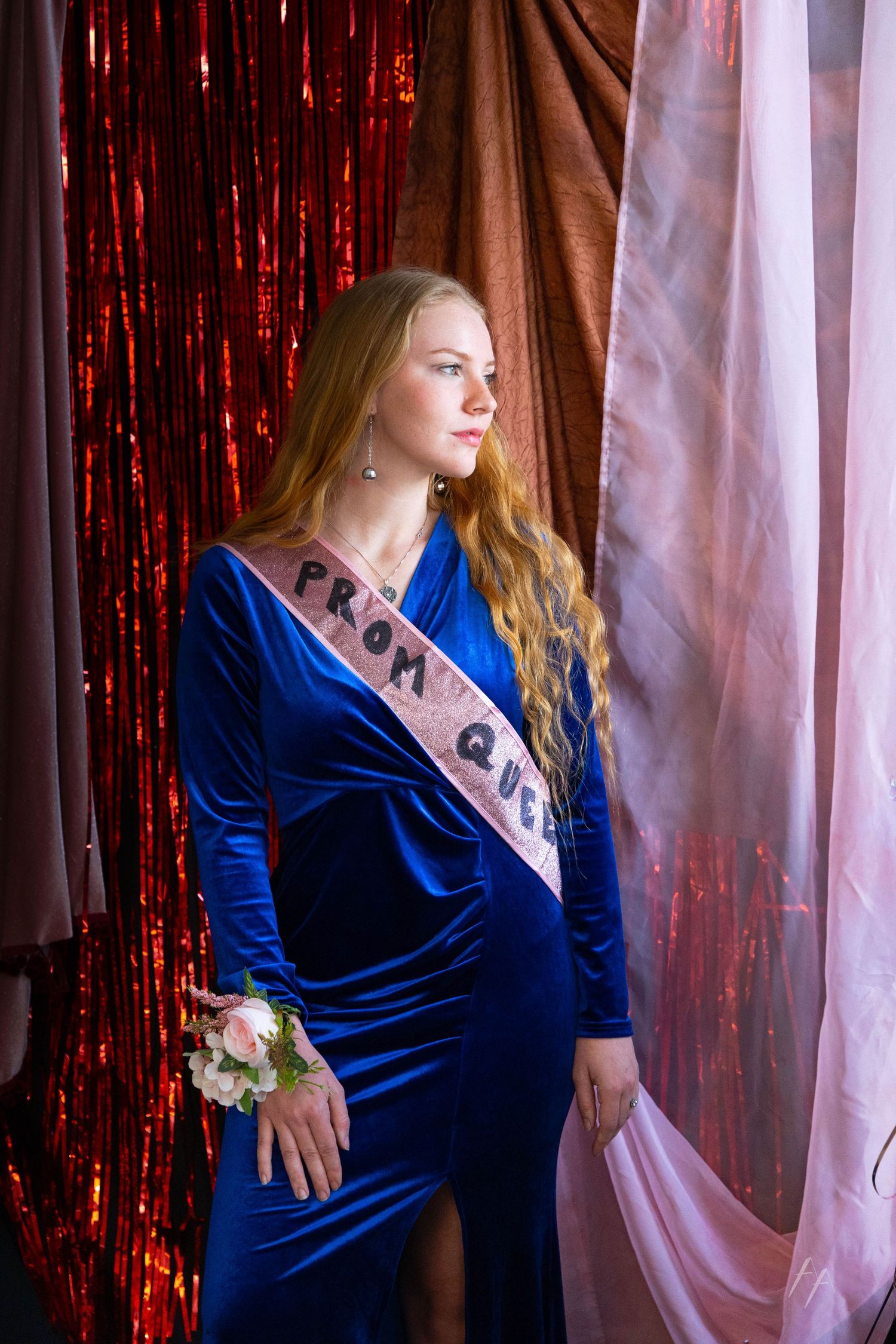 A woman in a royal blue velvet dress poses against a backdrop of red tinsel and white curtains.