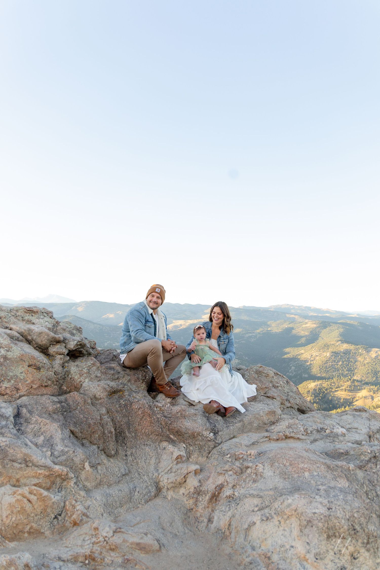 Couple sits together on rocky mountain overlook at sunset enjoying scenic mountain views in the distance.