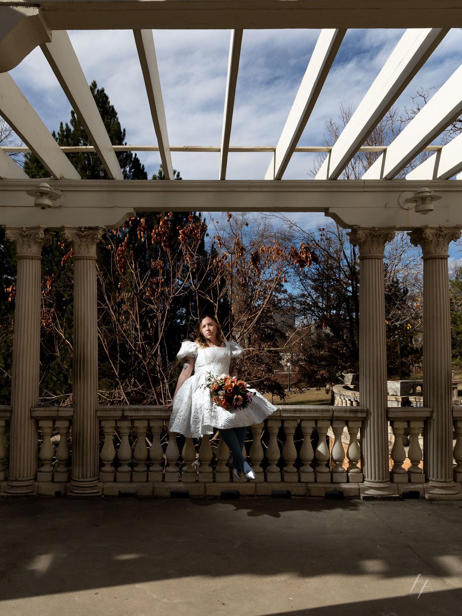 A white pergola structure with columns creates a shaded walkway against a blue sky backdrop.