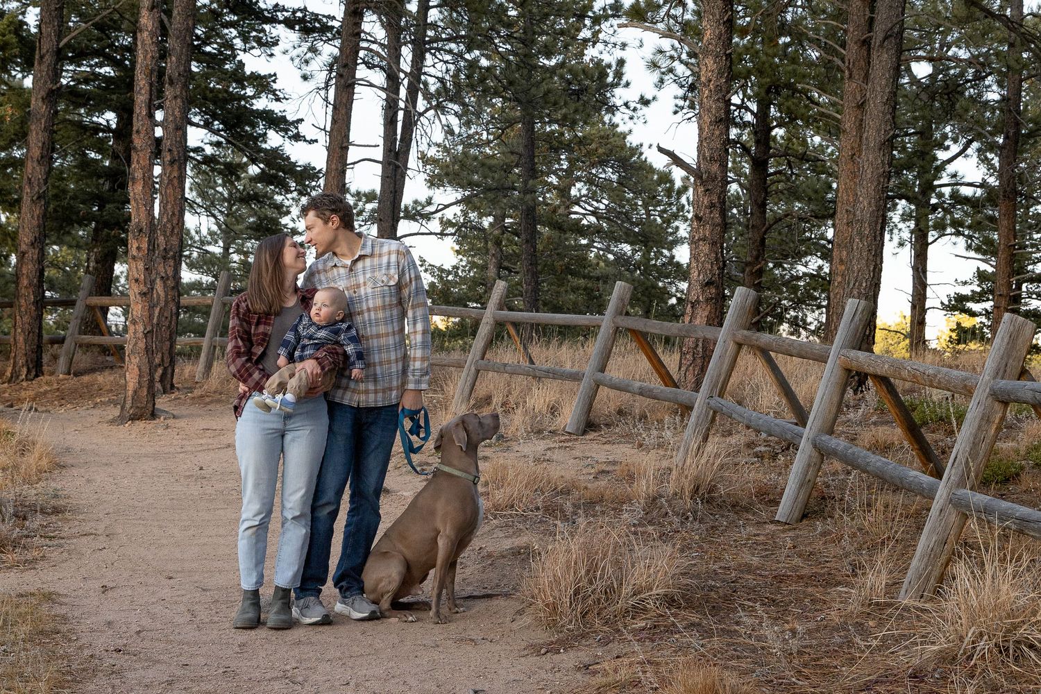 A couple stands together in a wooded area during an autumn engagement photo session in nature.