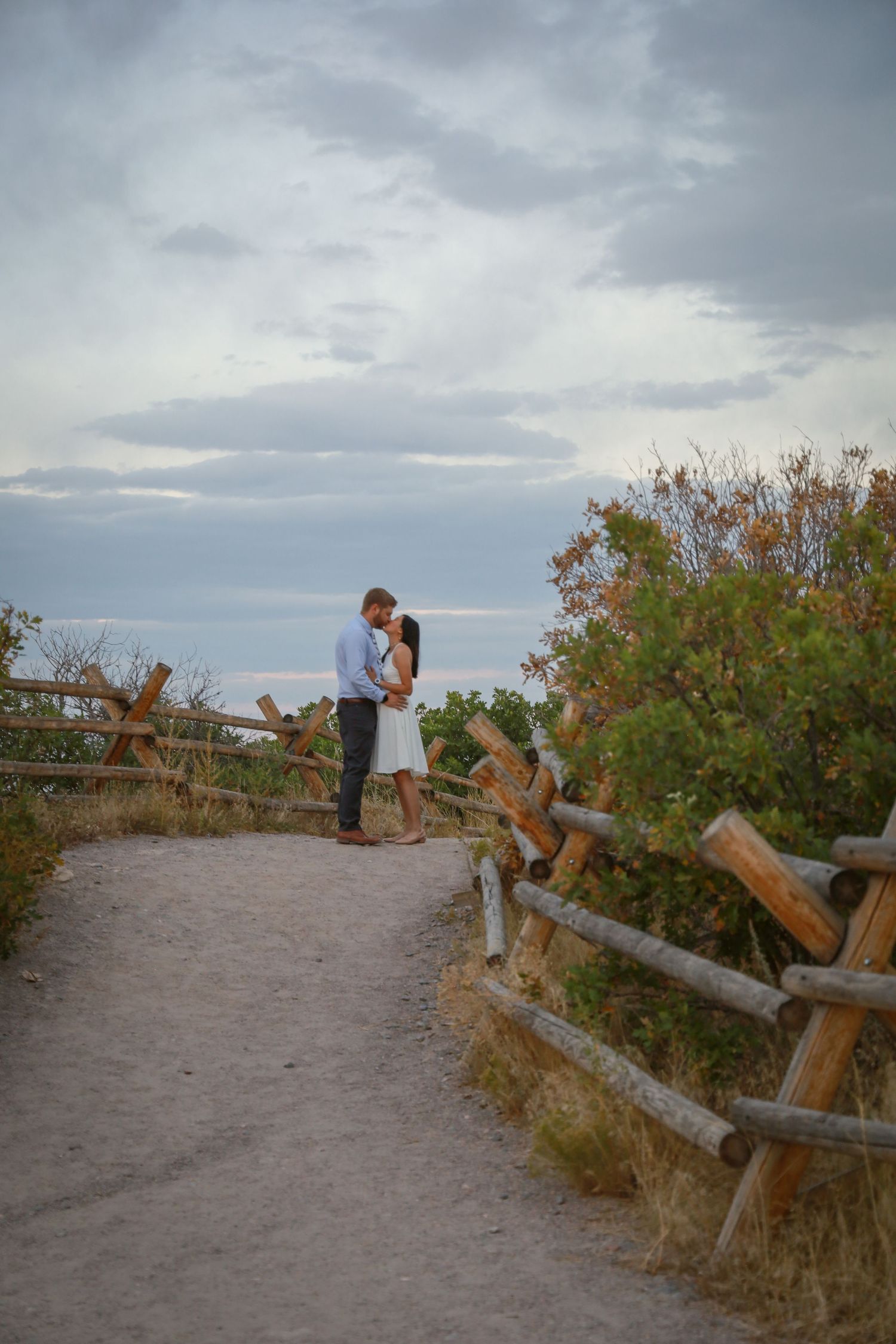 Couple standing on sandy path with rustic wooden fence at dusk.