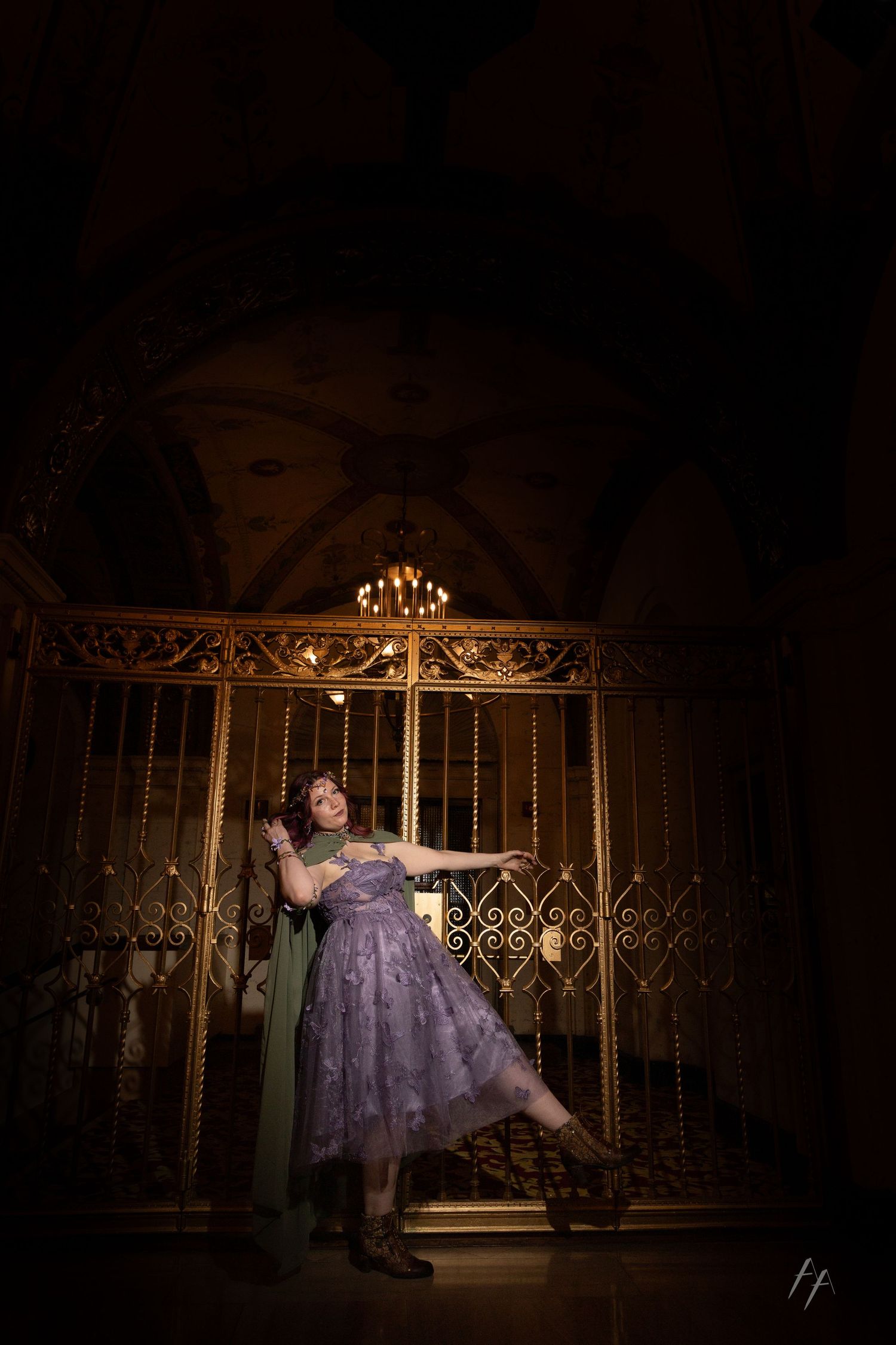 A person in a purple lace dress poses dramatically against an ornate gold gate in moody low-key lighting.