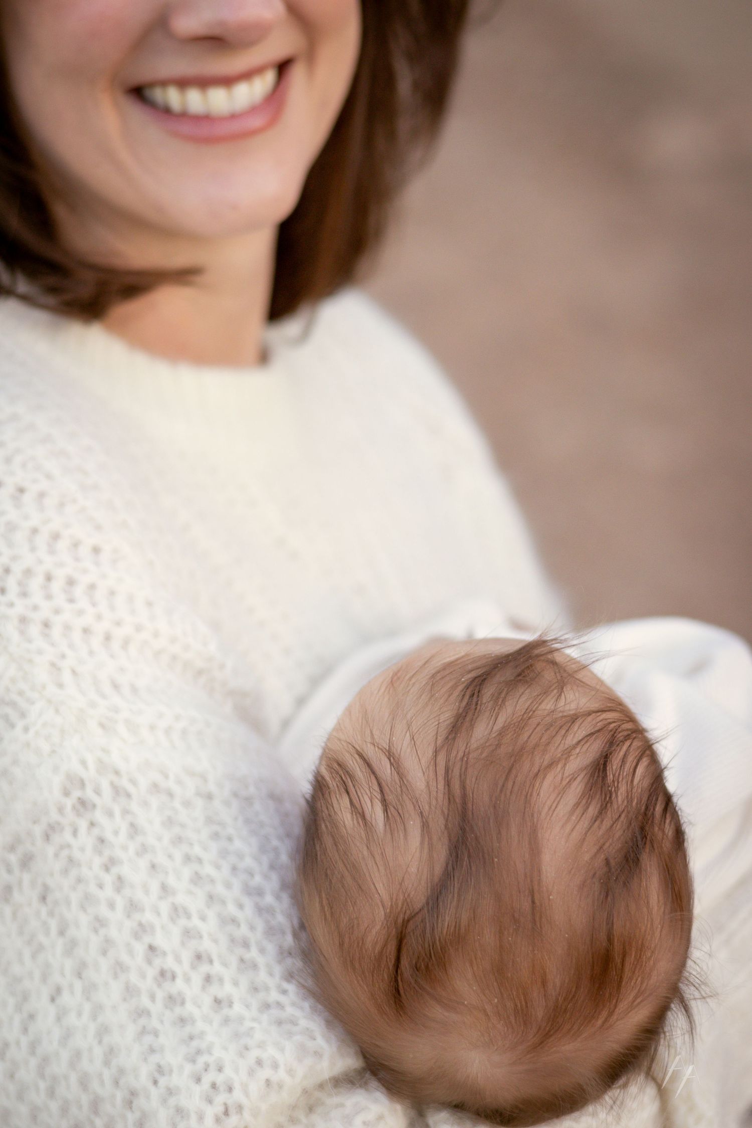 A person in a white knit sweater smiles warmly while holding a baby with brown hair.