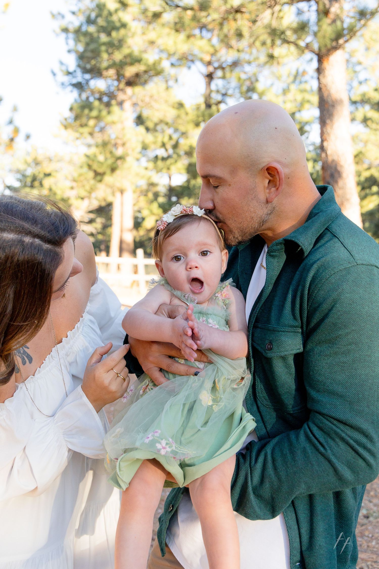 A sweet family moment outdoors in a sunlit forest setting with a baby wearing a mint green dress.
