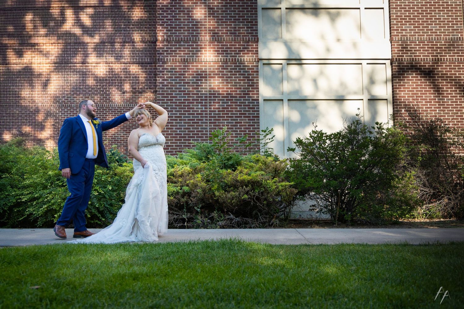 A couple in wedding attire shares a joyful moment together on a brick-lined garden path.