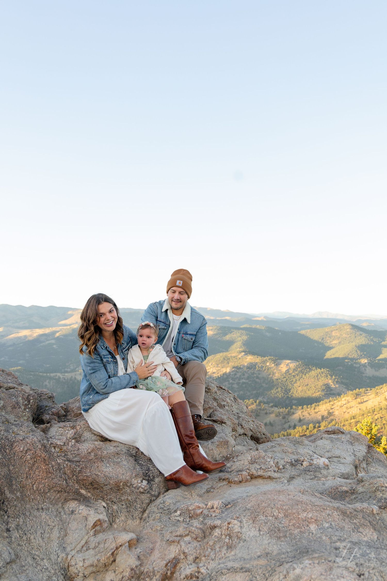 A couple sits together on a rocky mountain overlook during sunset in the wilderness.