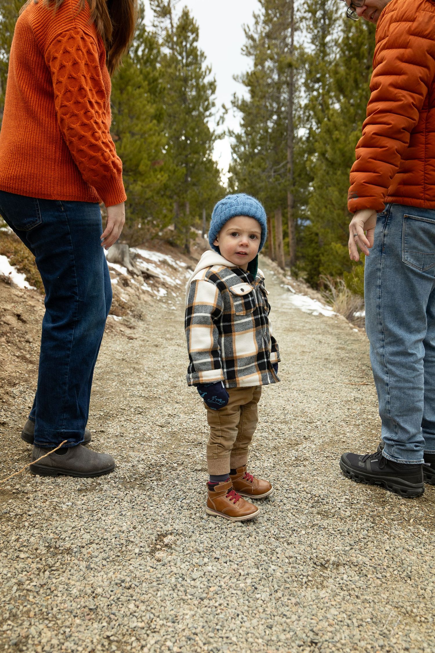 Close-up view of feet showing a parent and child wearing winter boots and jeans standing on gravel ground.