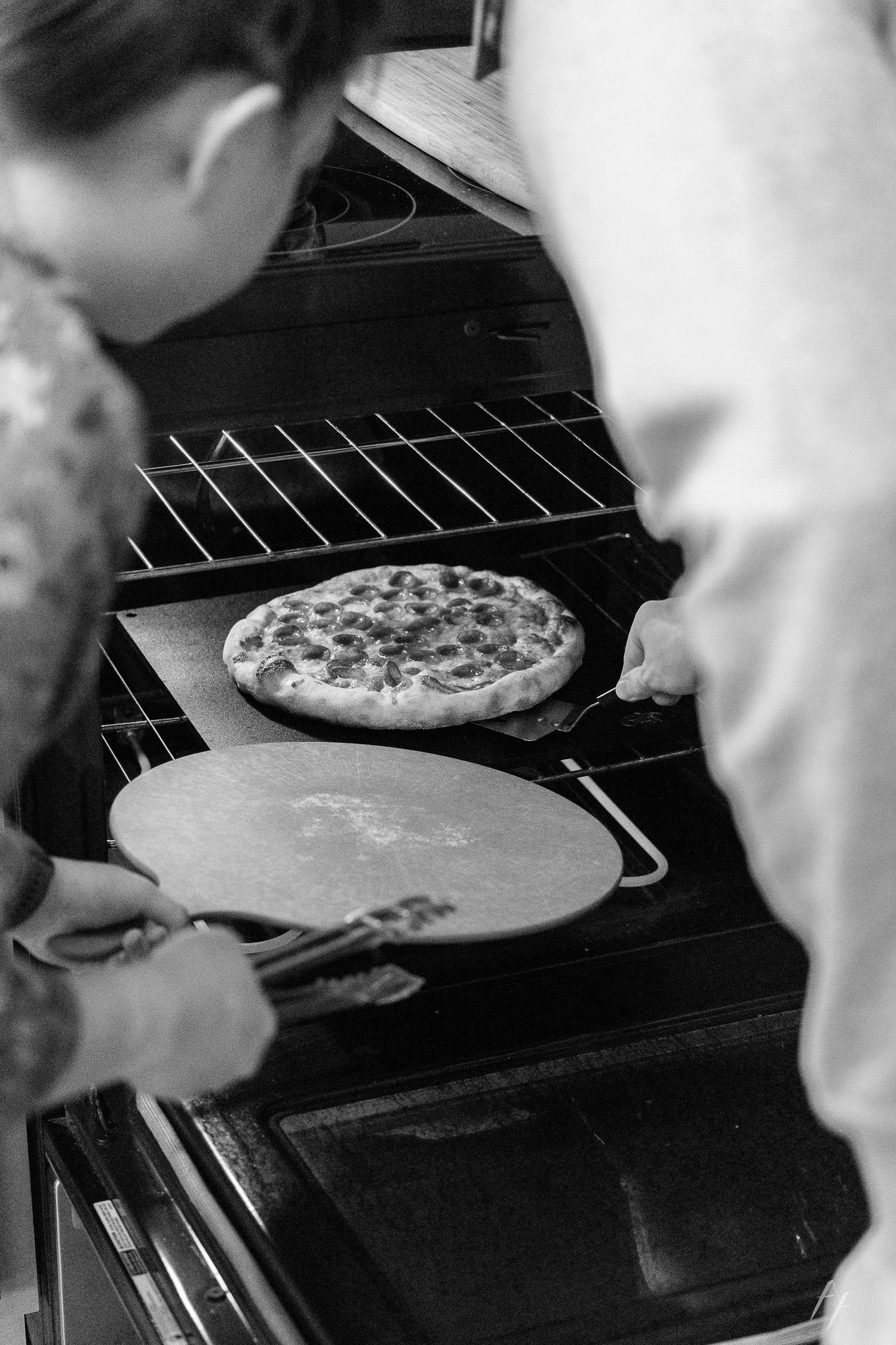 Pizza dough being prepared and placed in an oven on a pizza stone.