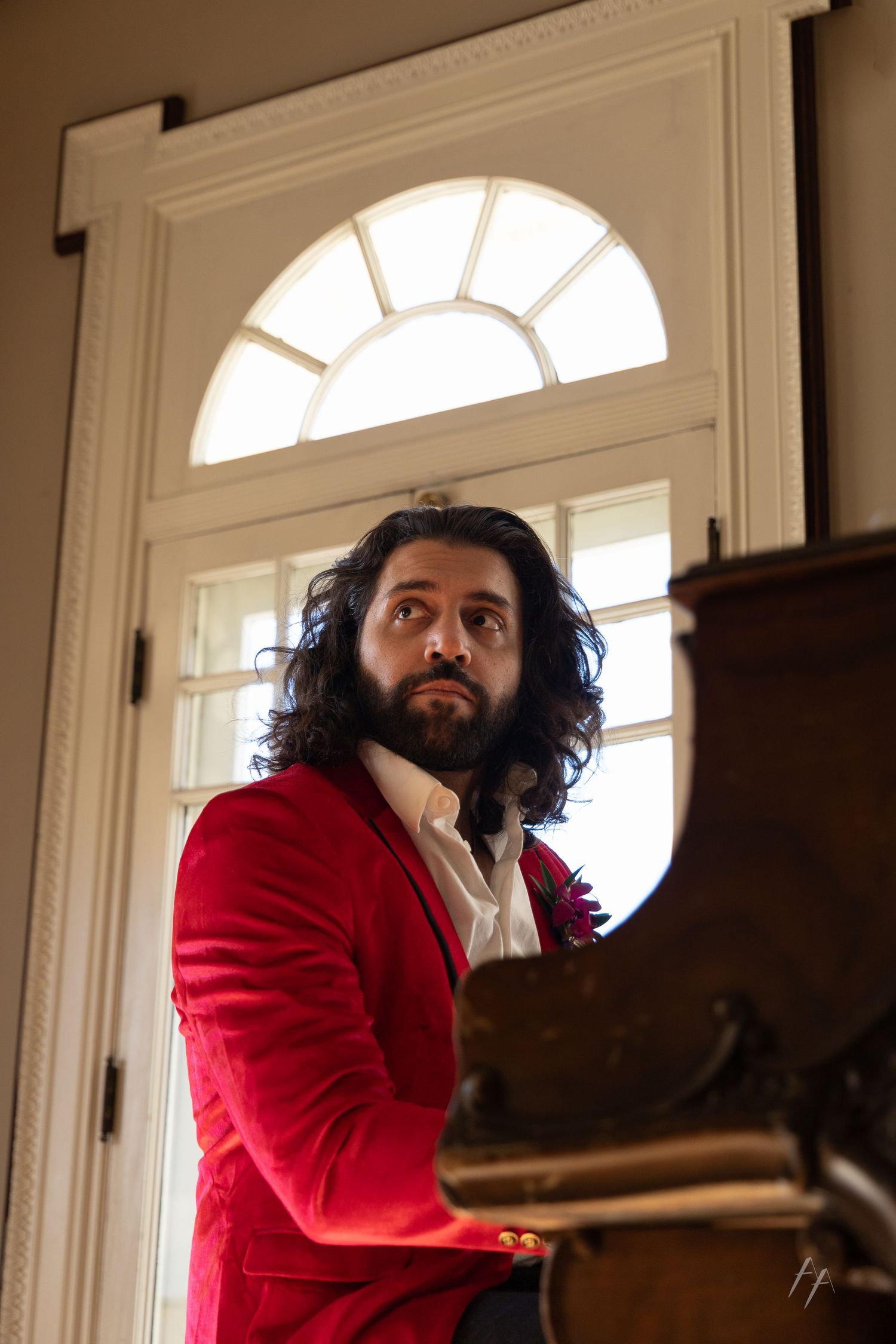 A person in a bright red jacket sits thoughtfully by large arched windows in a sunlit room.