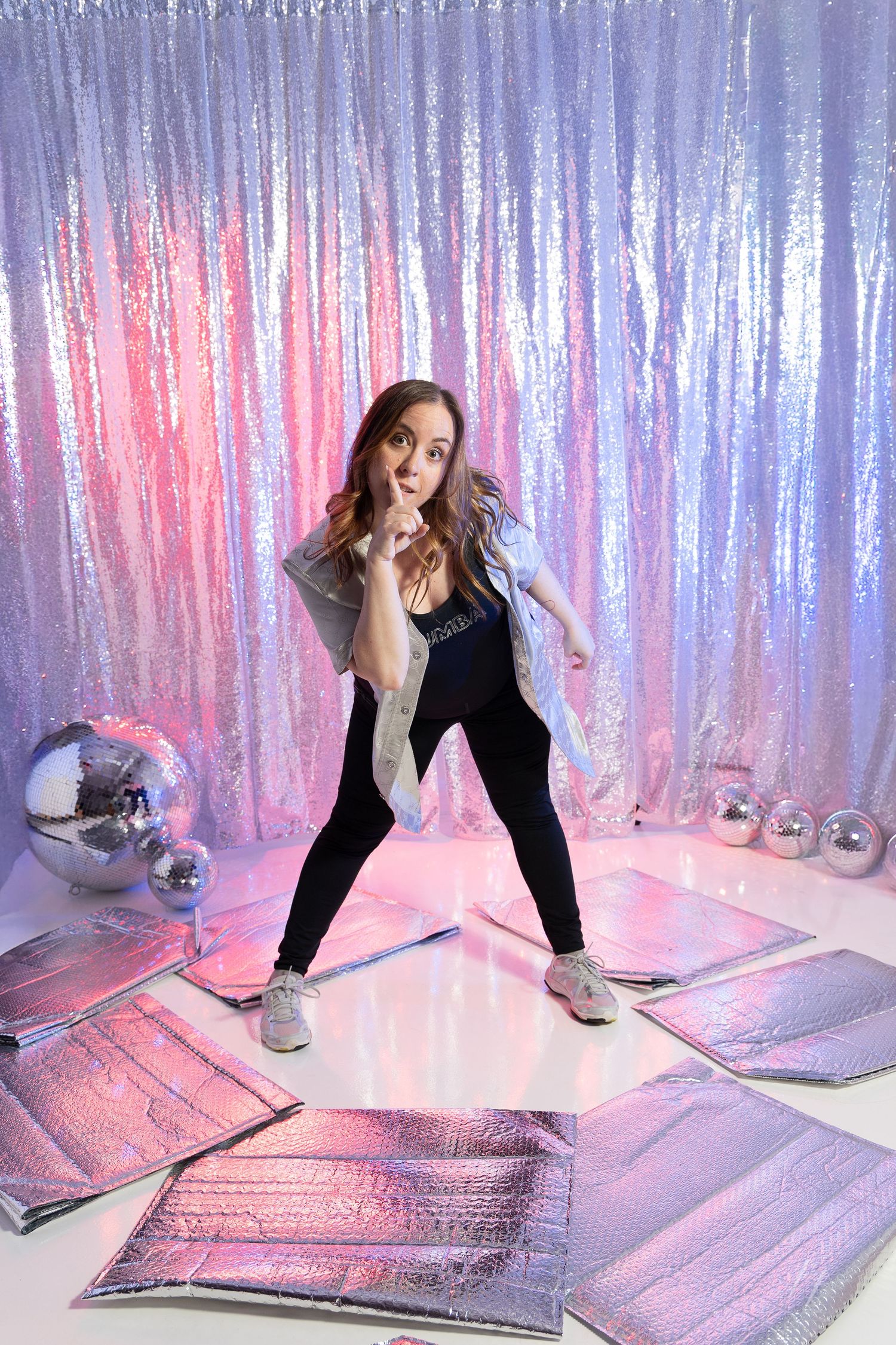 A person in a black top and light pants crouches down to adjust reflective metallic mats on a pink and purple lit floor.