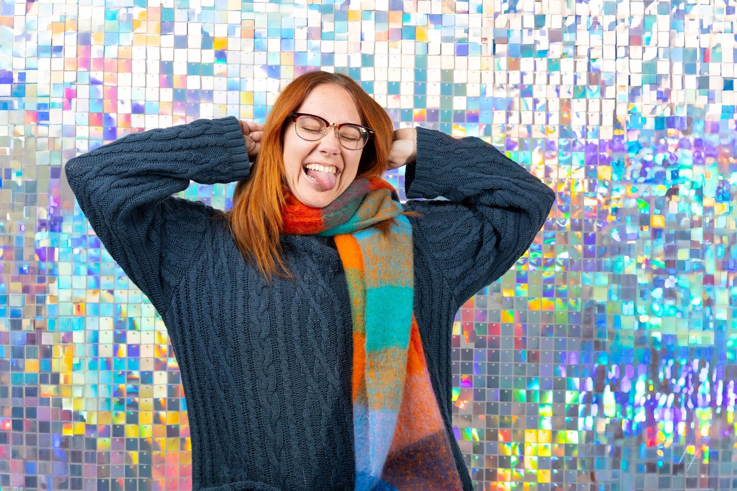 Person in gray sweater poses against colorful mosaic wall background making playful expressions.