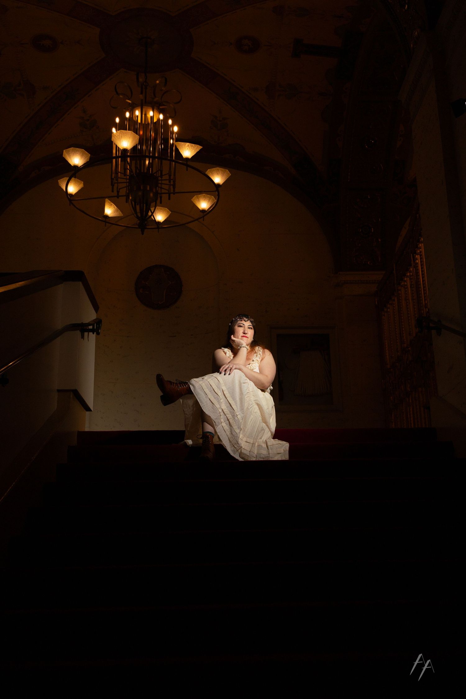 A couple dancing in a dimly lit ballroom with elegant chandeliers casting a warm glow overhead.