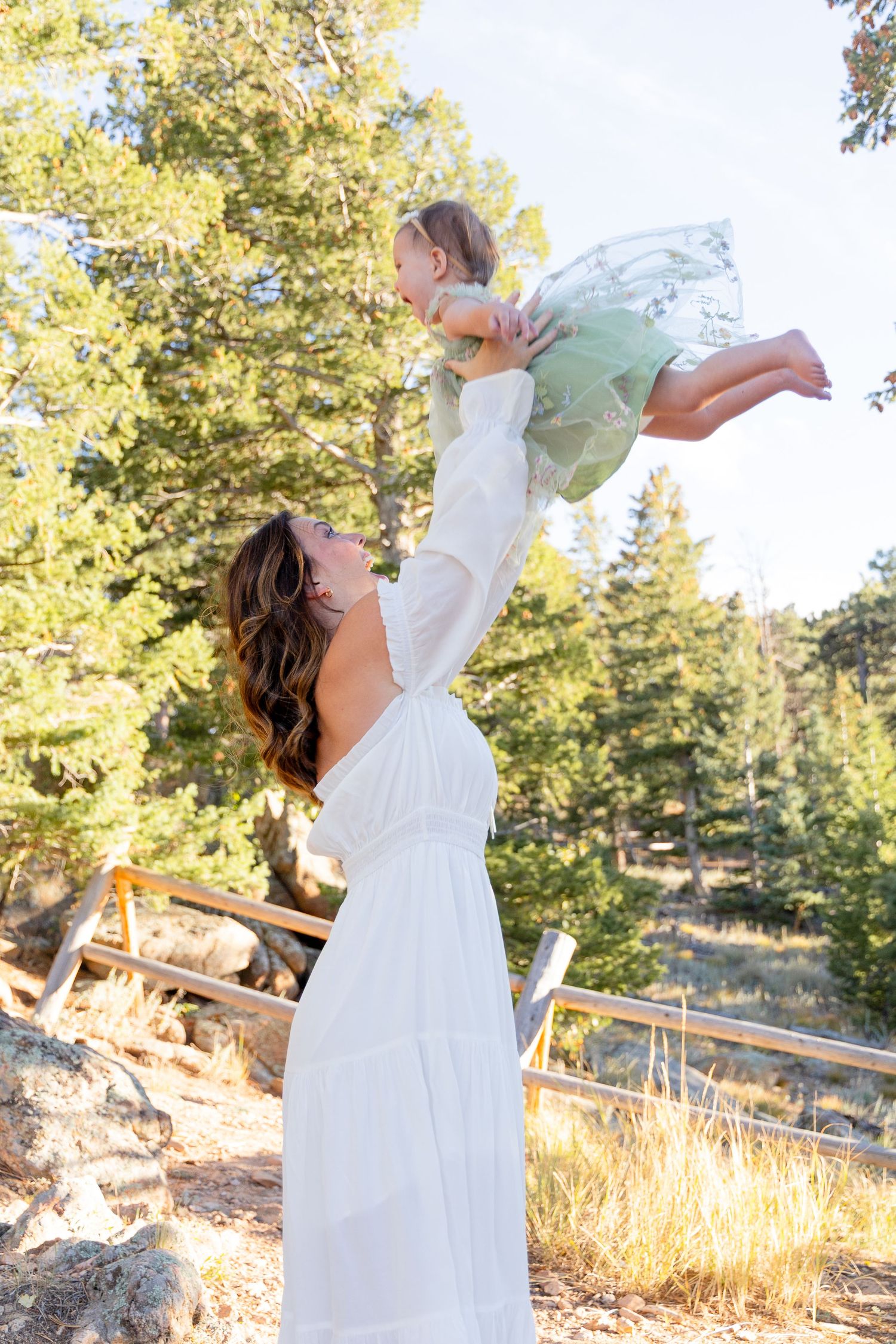 A person in a flowing white dress twirls gracefully in a sunlit outdoor setting with trees and golden grass.