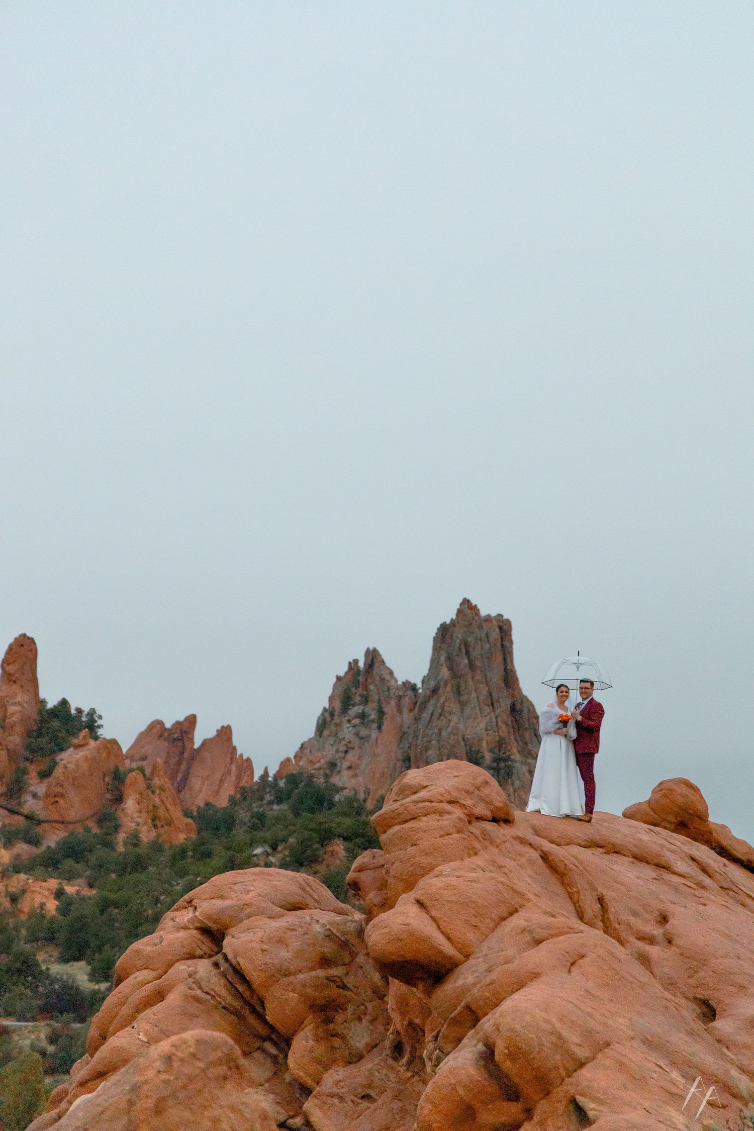 Couple eloping atop red rock formations at Garden of the Gods, Colorado, holding umbrella on overcast day.