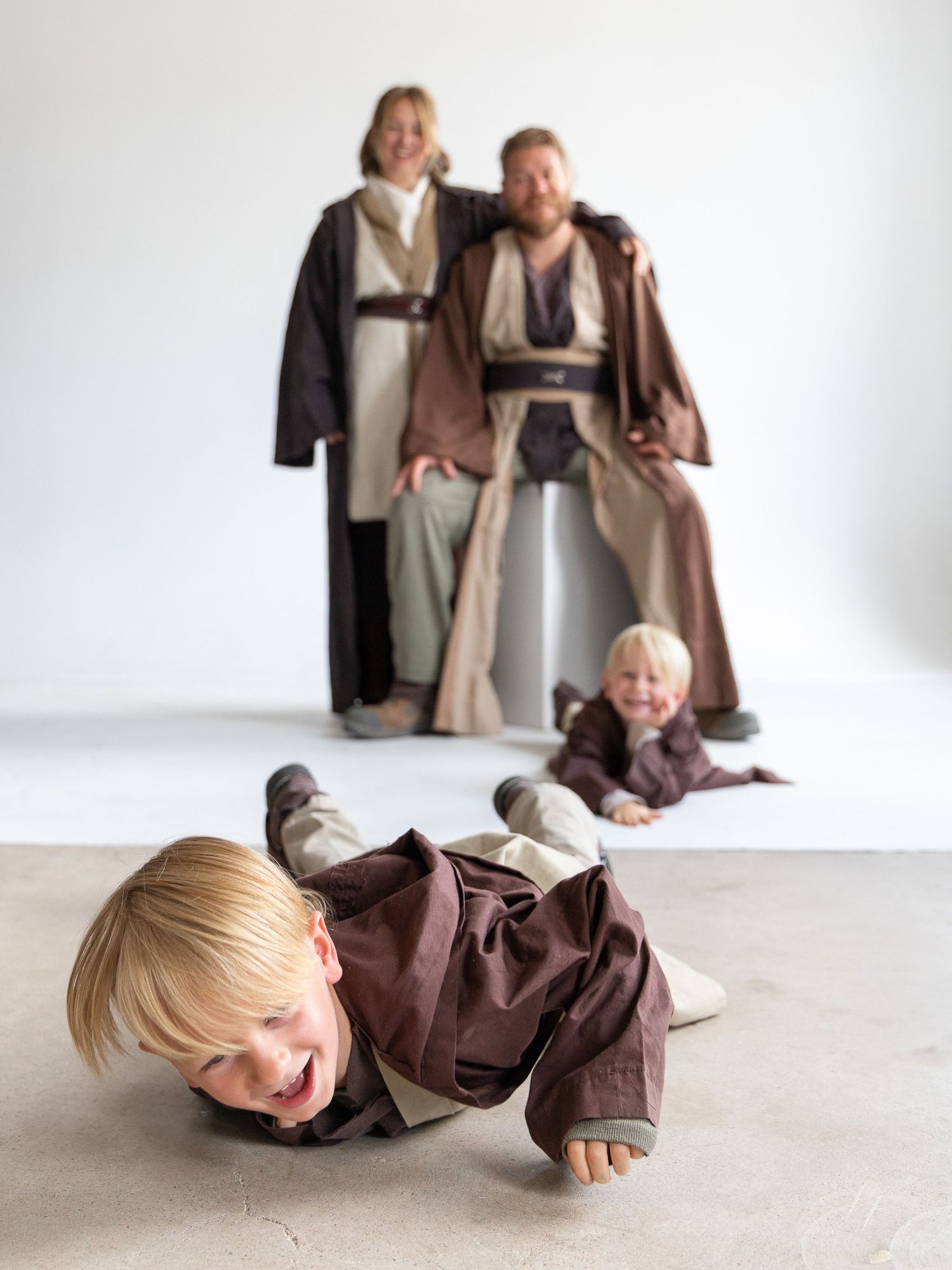 Multiple shots of people lying on a white floor wearing brown Jedi-style costumes.
