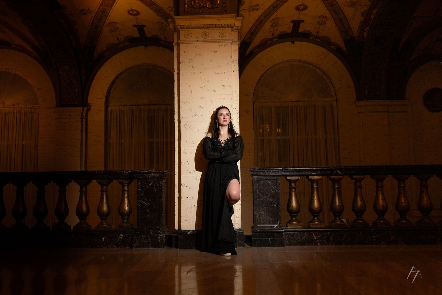 A figure in a long black dress stands dramatically in an arched doorway of a historic building with ornate architecture.