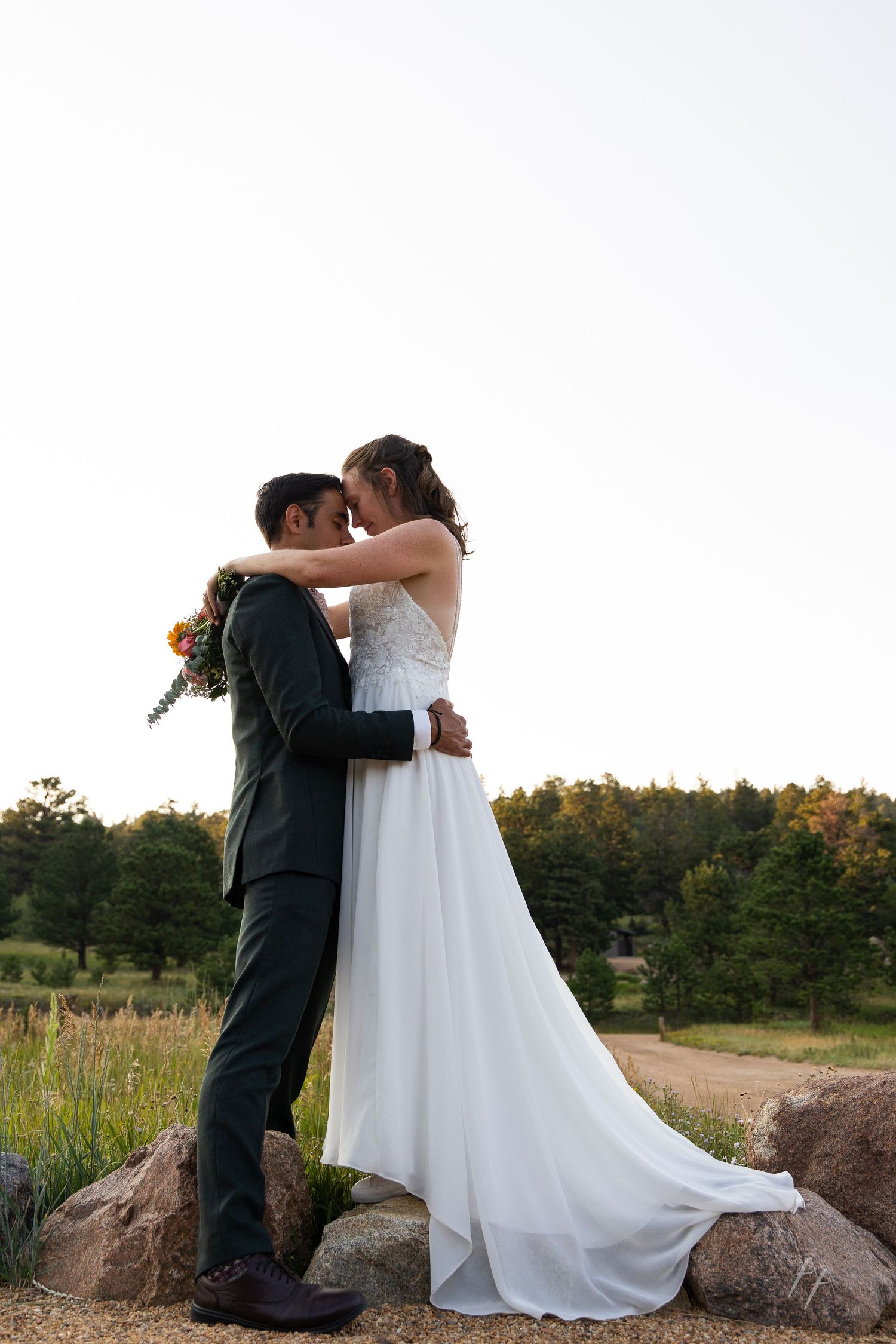 Bride and groom share a romantic moment outdoors, with the bride in a white gown holding a colorful bouquet.