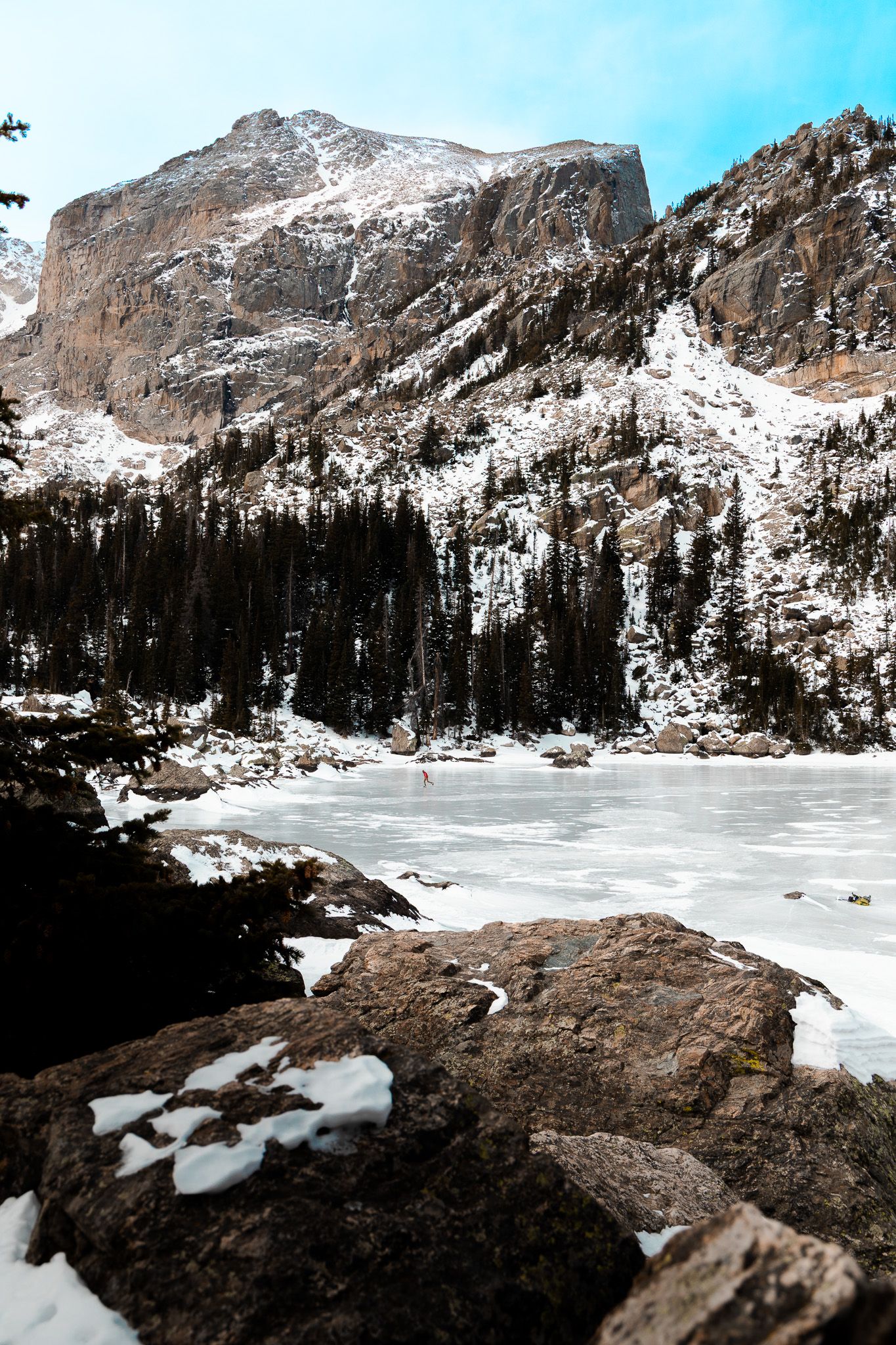 Frozen mountain lake surrounded by snow-covered peaks and evergreen forest. Rocky Mountain National Park
