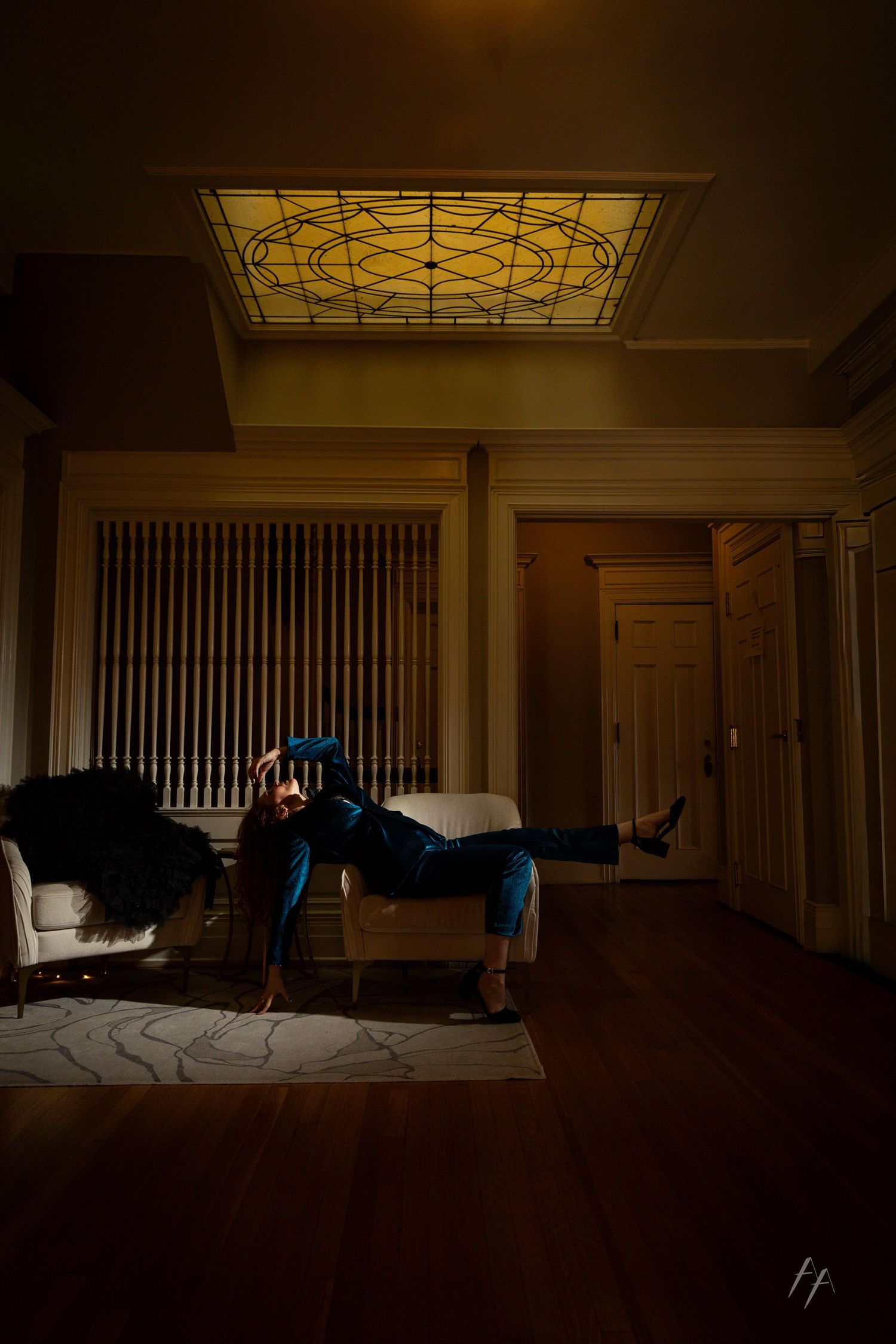 A moody interior scene with a stained glass skylight illuminating a person lounging on an antique chaise lounge.