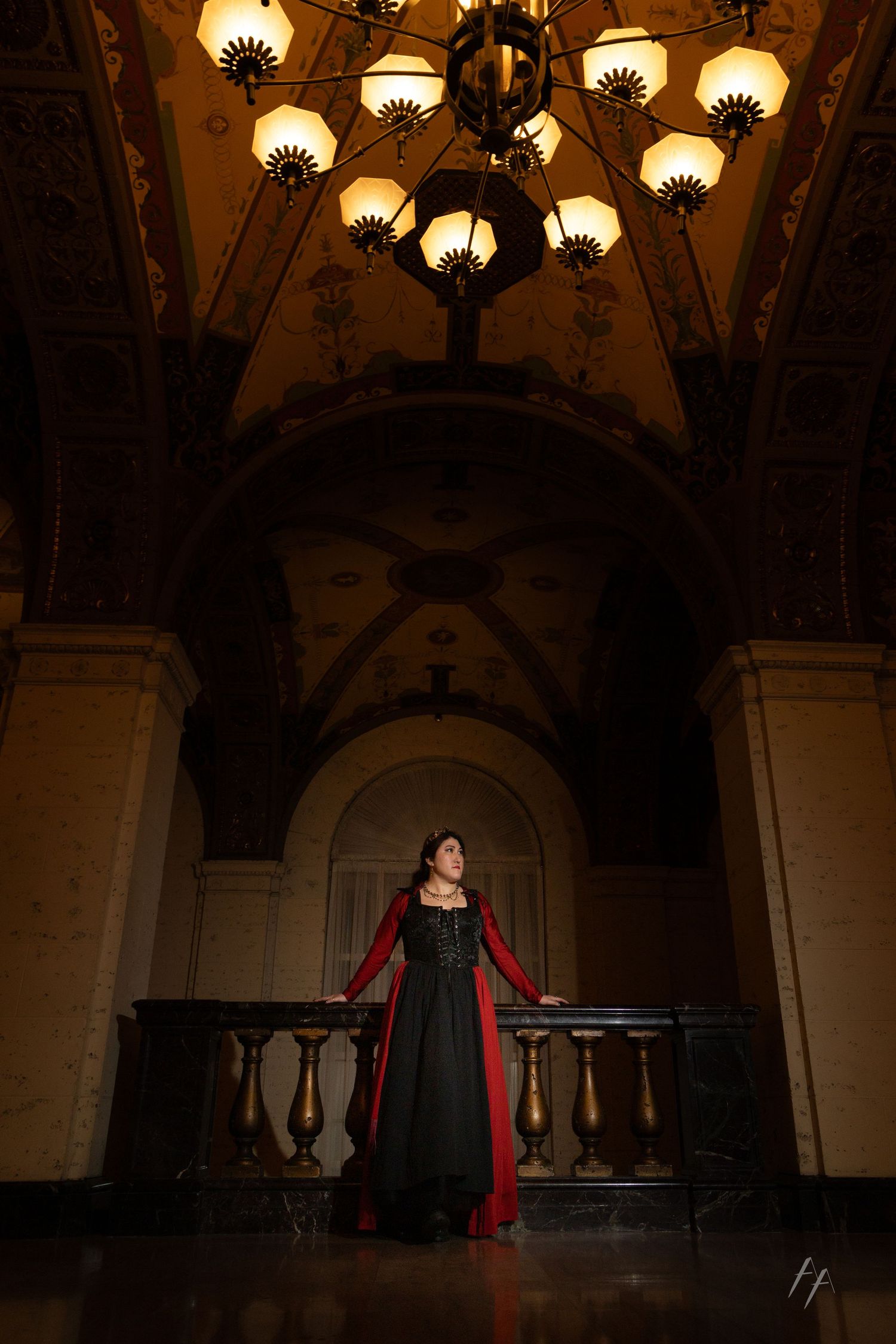 A dramatic scene in an ornate historic theater with chandeliers and a flowing red scarf in motion.