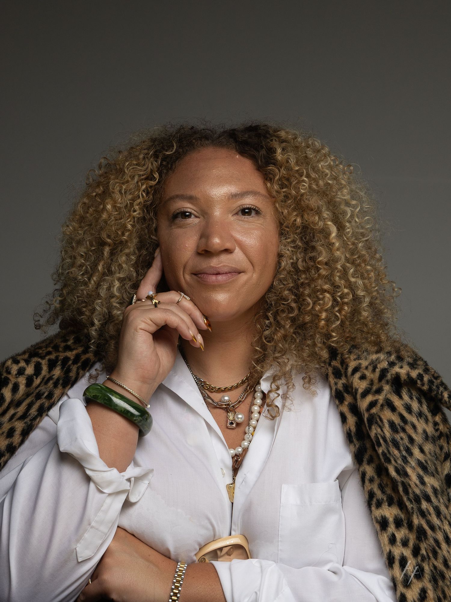 Portrait of someone wearing a white button-down shirt and leopard print jacket, with curly blonde hair and layered necklaces.