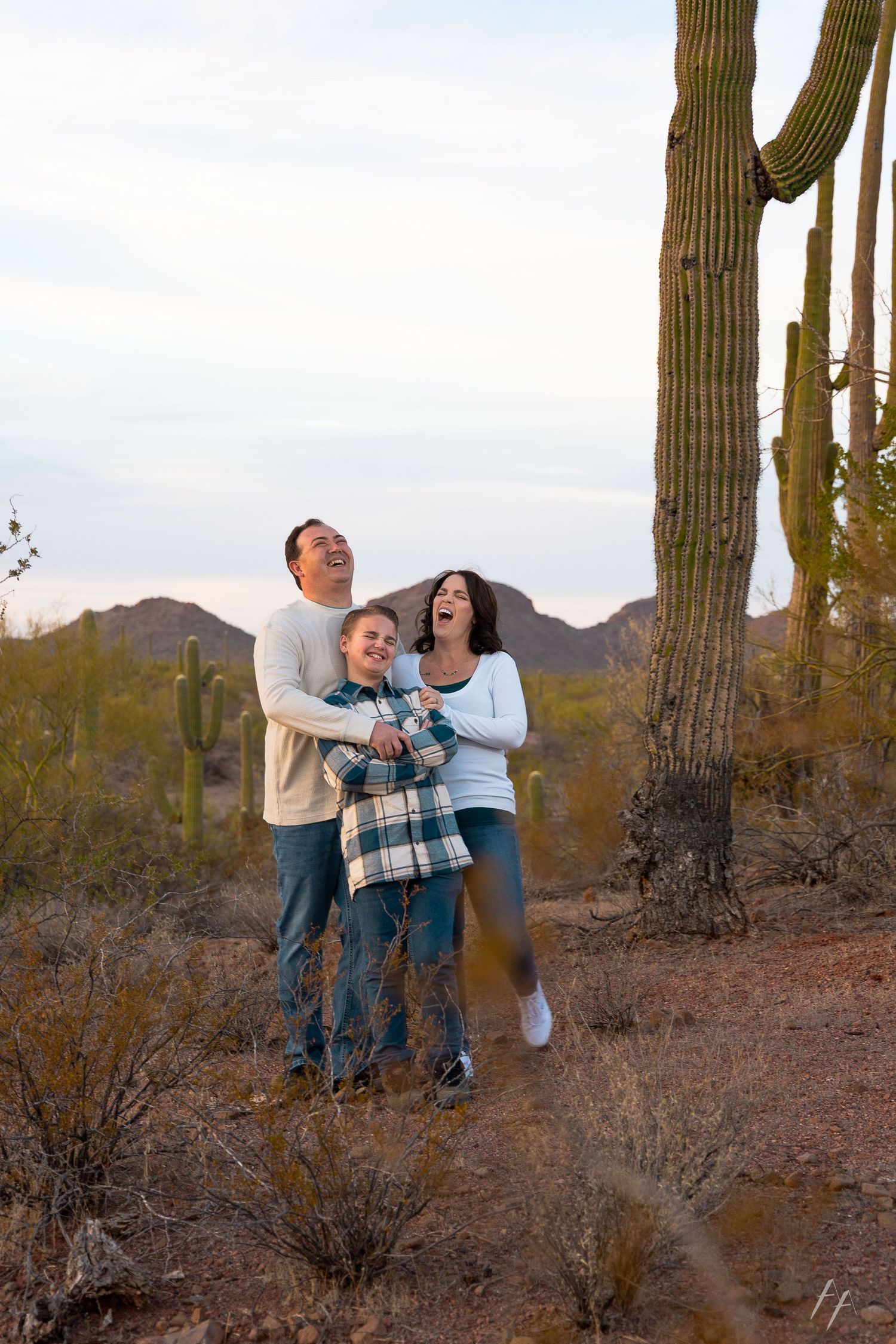 Family enjoying a playful moment together in a desert landscape with tall saguaro cacti and mountains in the background.