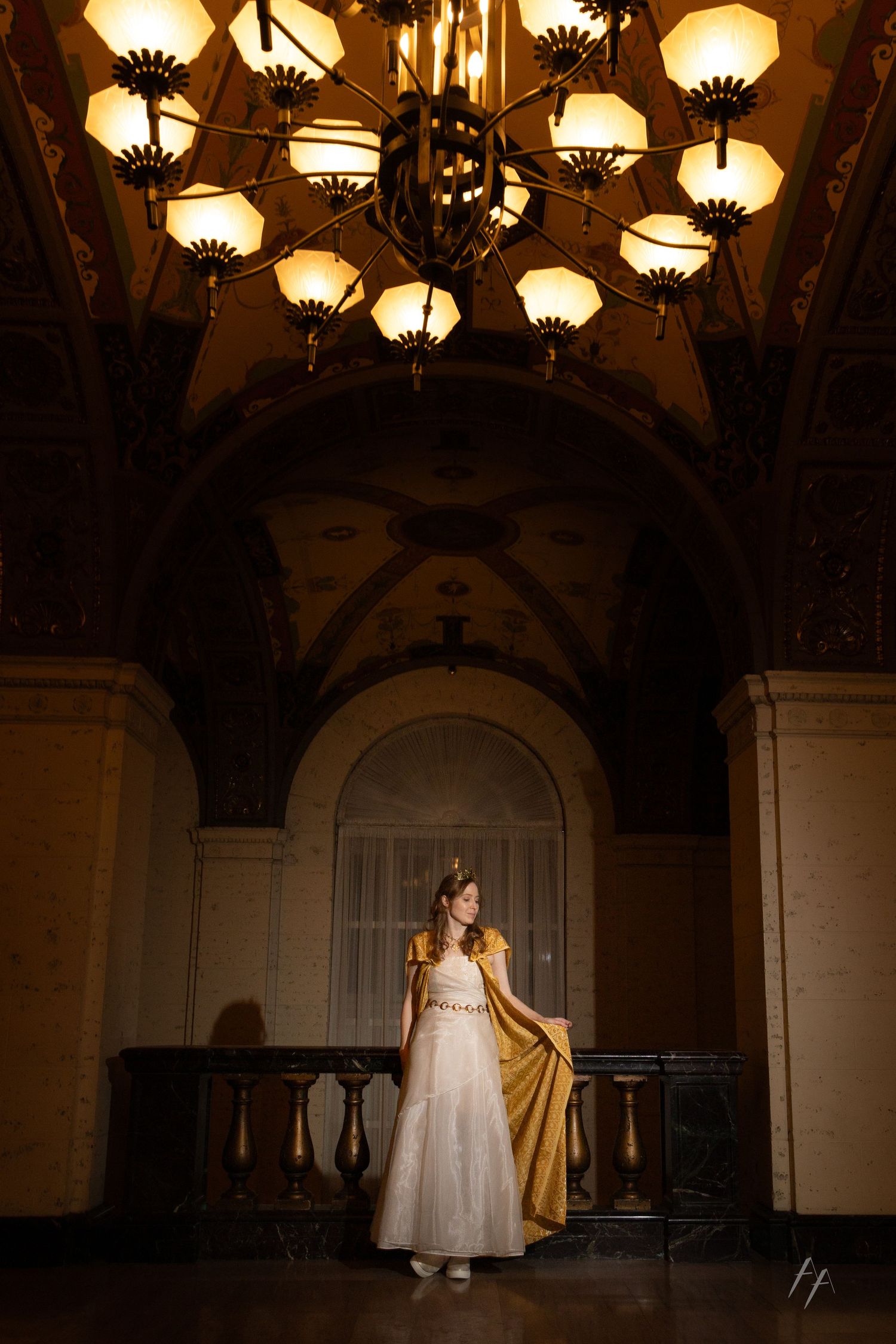 Two children in white dresses twirl and dance beneath ornate vintage chandeliers in a grand hallway.