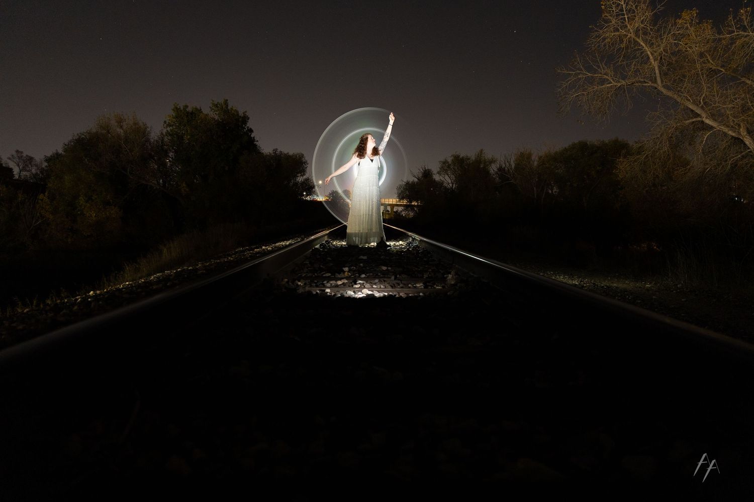 A white barn owl perched on a branch at night with its wings spread wide in a dramatic pose.