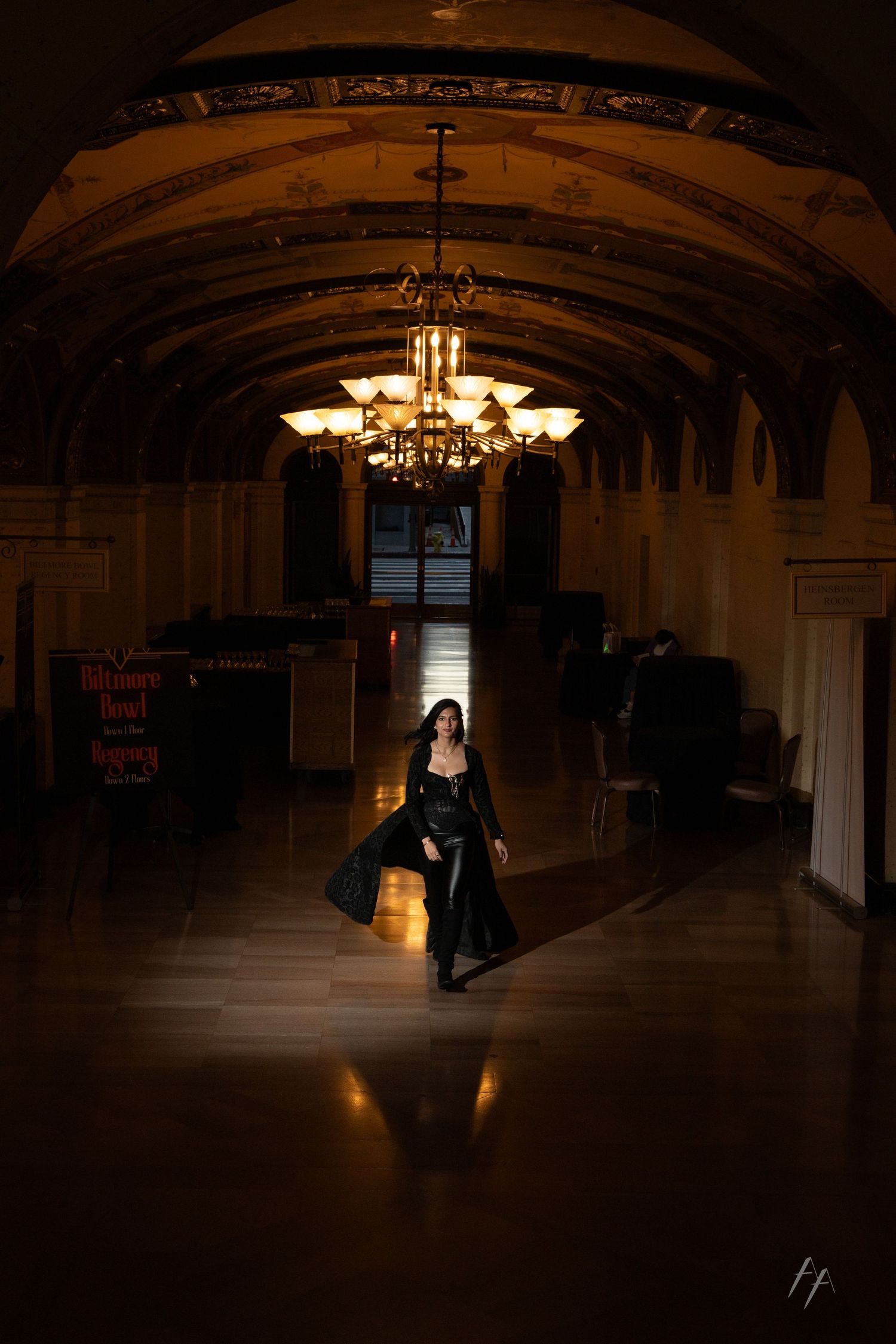 Dramatic silhouettes dance in a dimly lit historic ballroom with arched ceilings and vintage chandeliers.