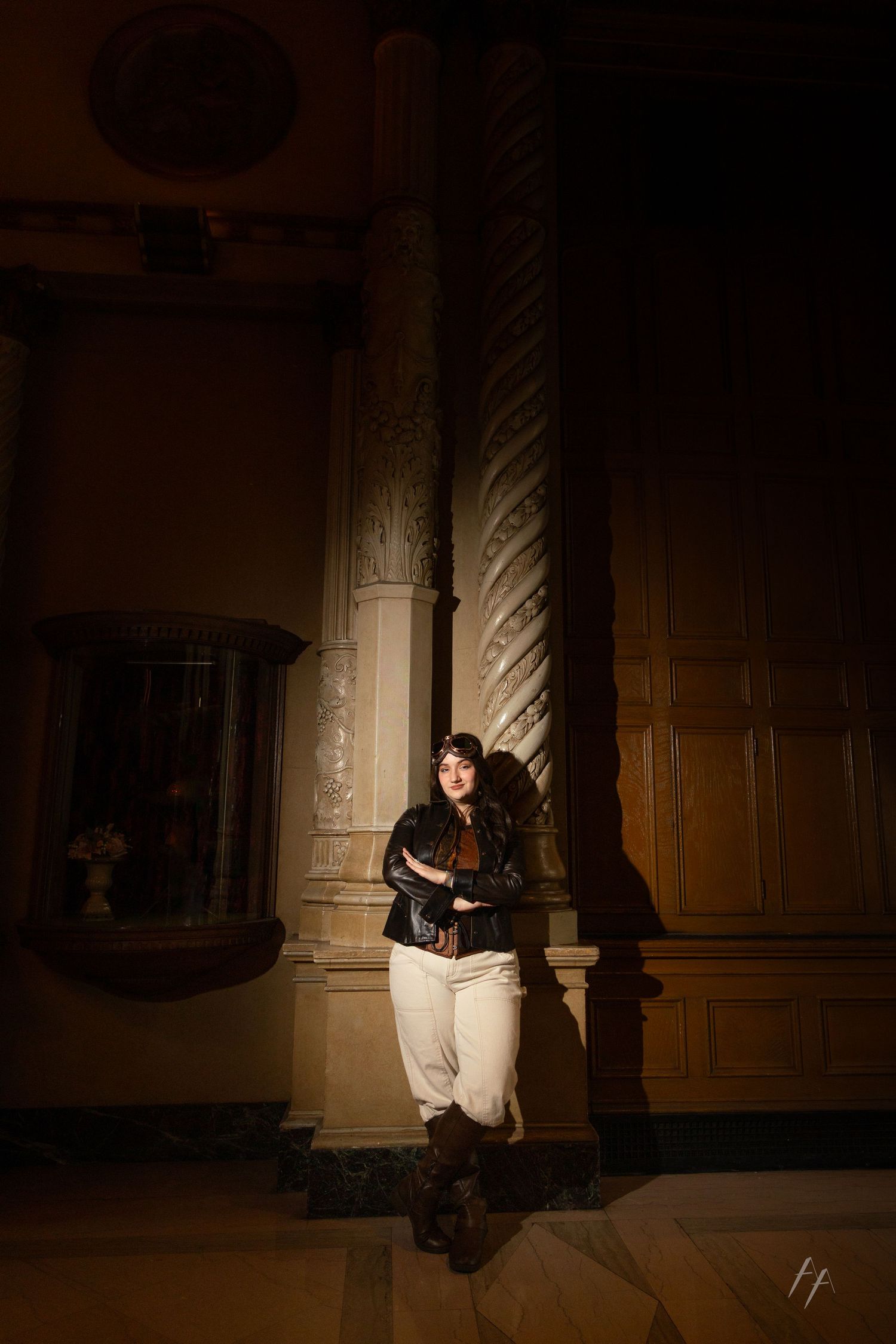 A person sits in a dark hallway illuminated by dramatic lighting while reading against an ornate wooden wall.