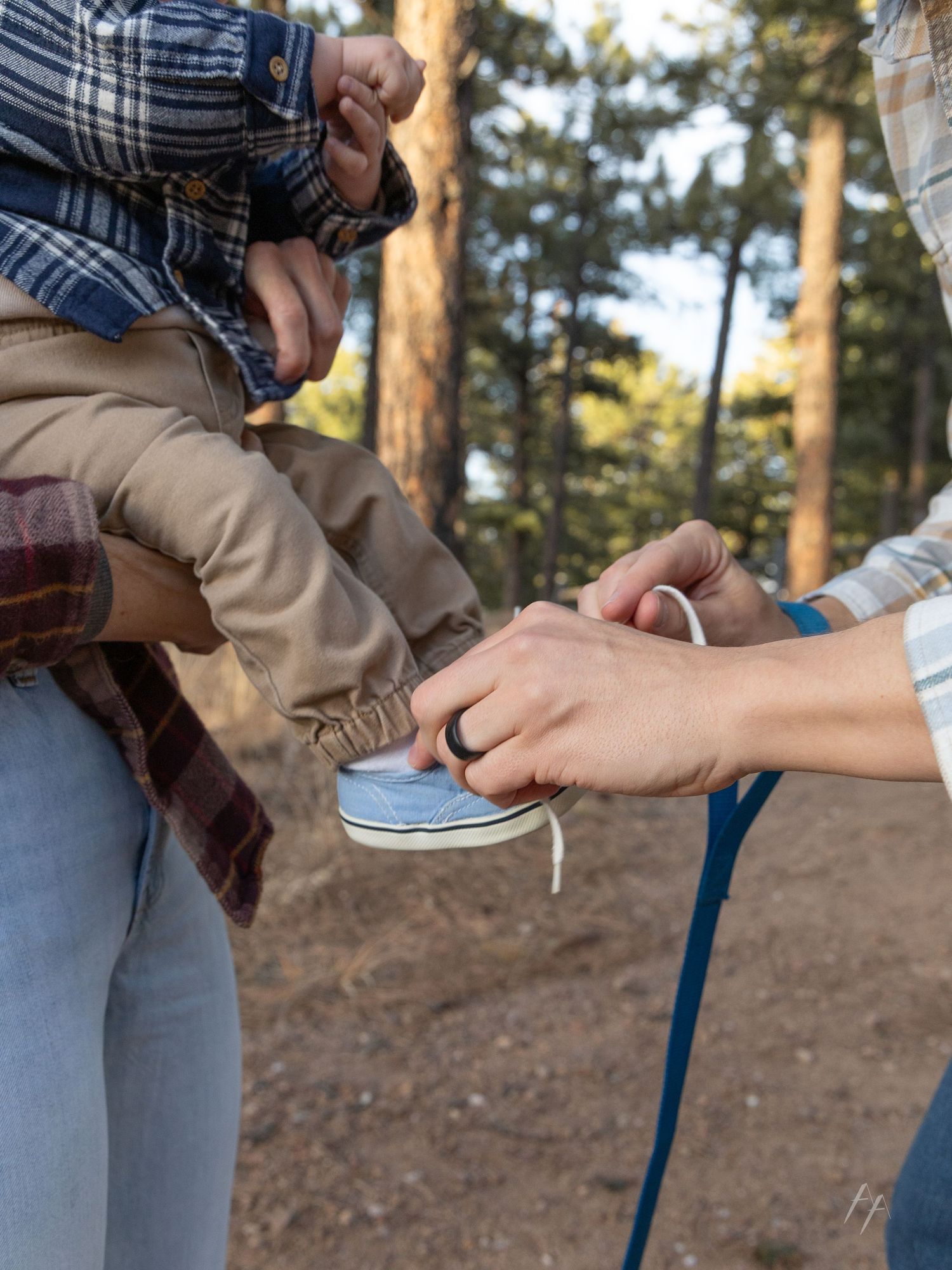Close-up series showing a person putting on a plaid shirt button by button in a wooded outdoor setting.