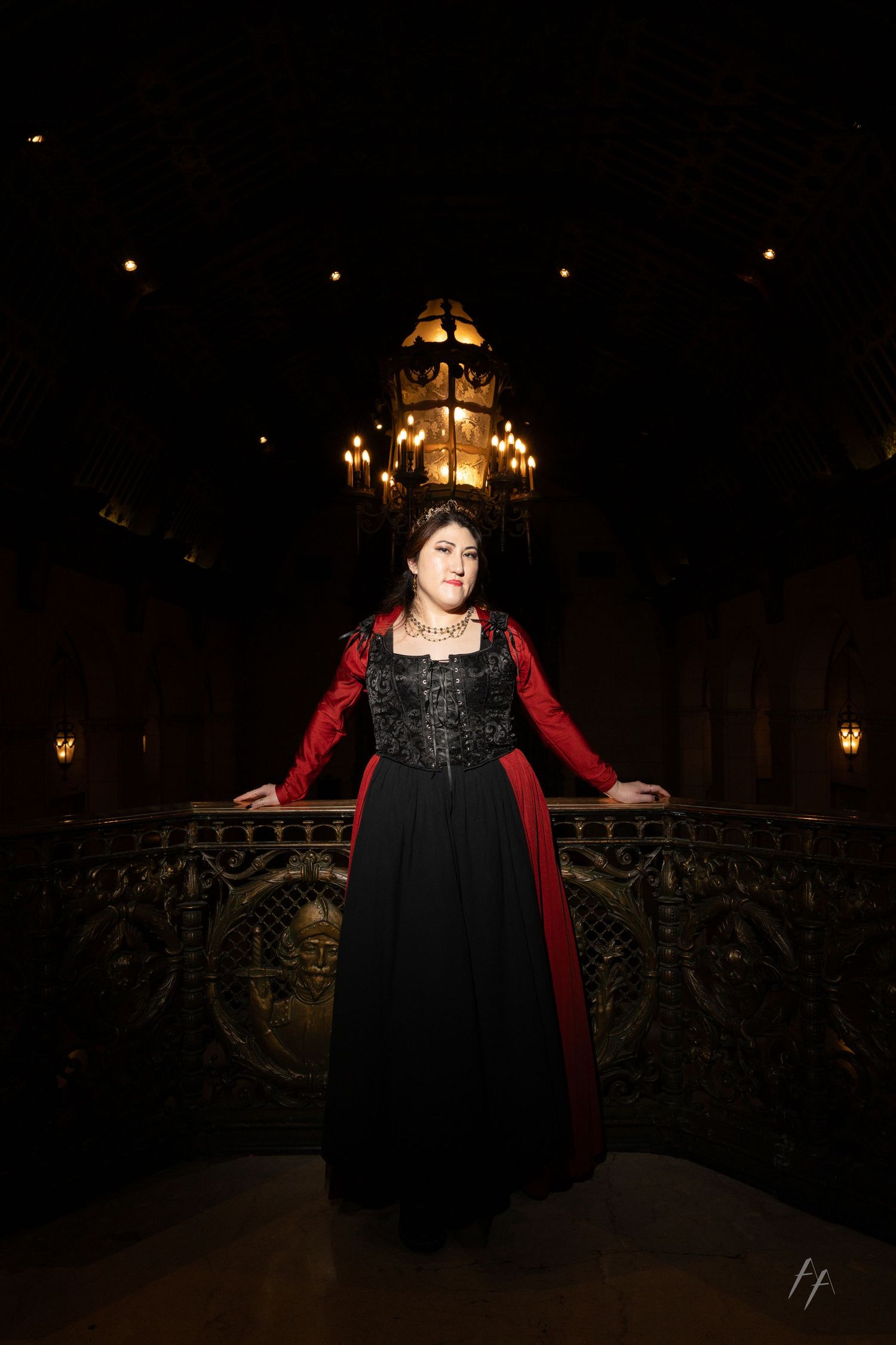 A figure in a black dress and red velvet cloak stands on a dark bridge with ornate railings and glowing lights.