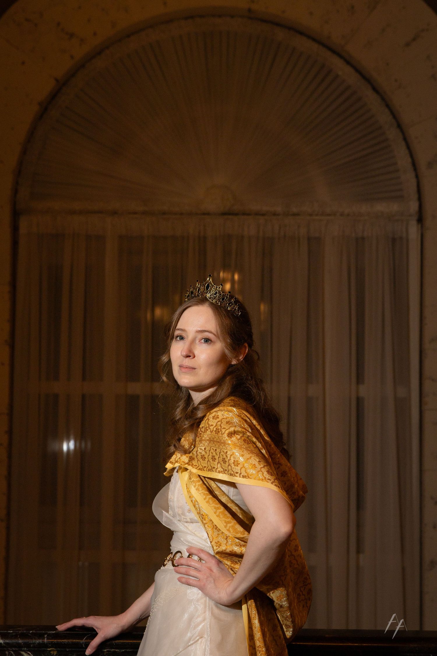 A person in a gold cape and crown poses regally against a curtained archway in warm lighting.