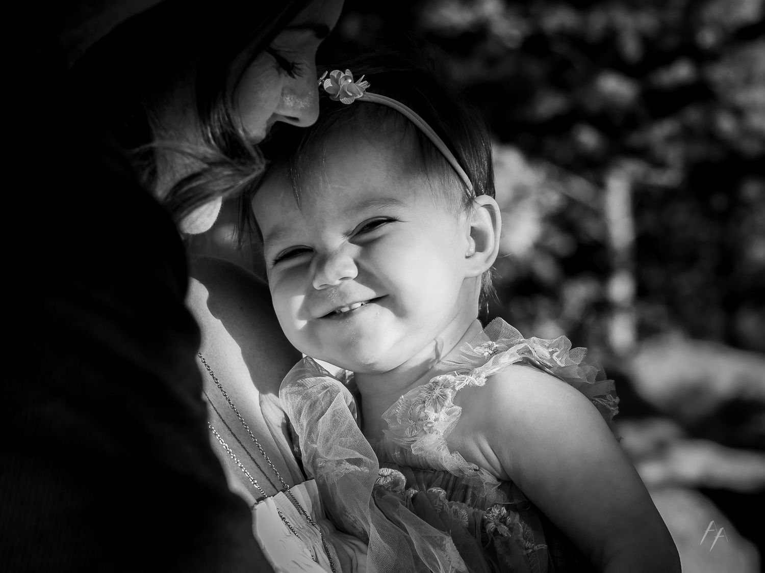 A happy child wearing a floral dress and headband smiles brightly in black and white portrait photography.