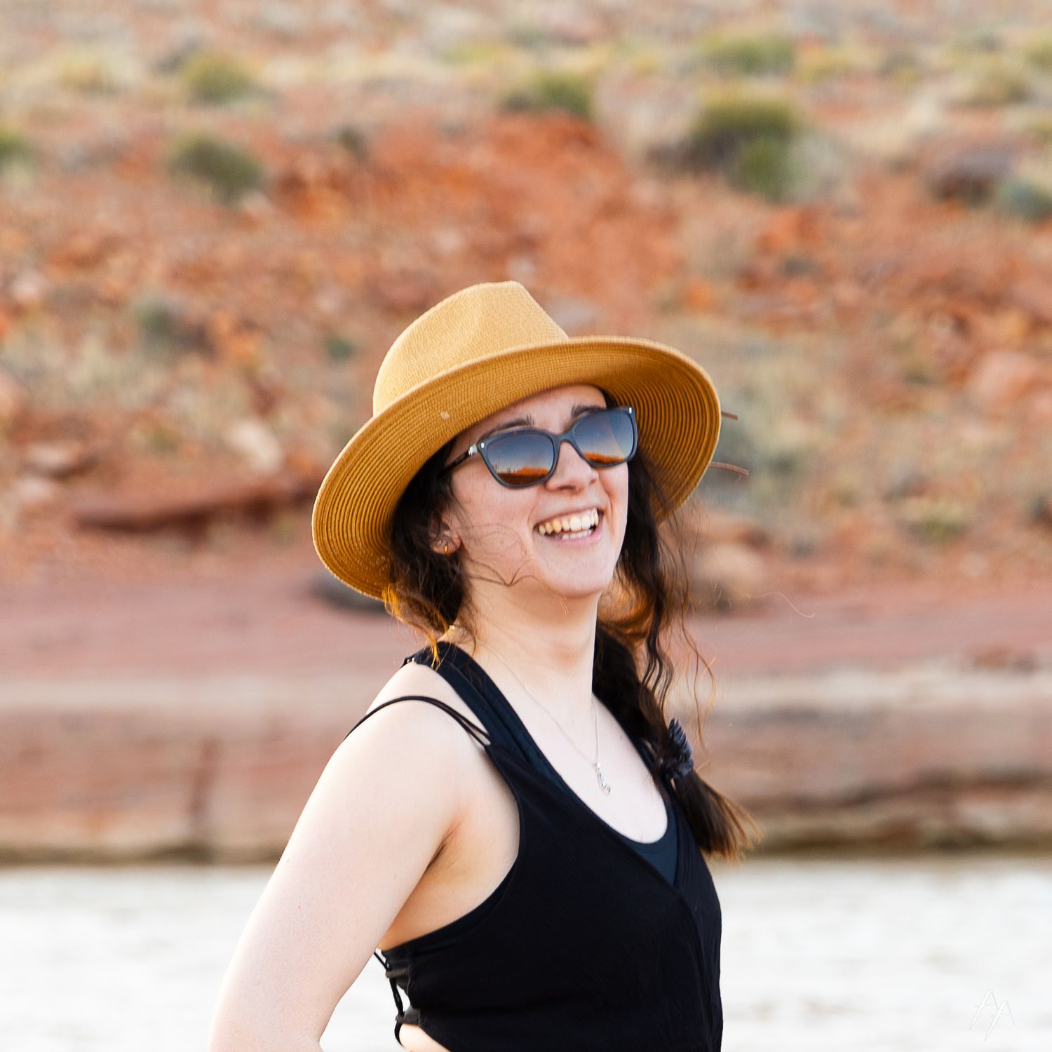 Person in black tank top and tan sun hat enjoying a sunny desert landscape.