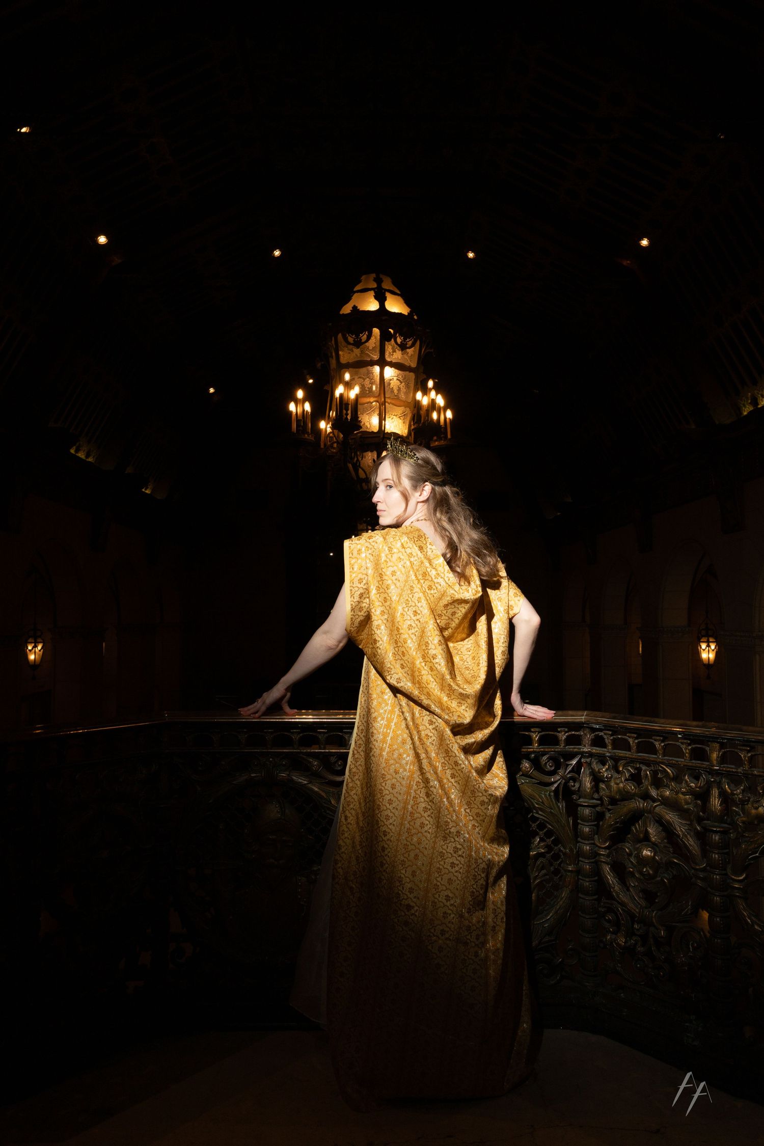 A figure in a golden dress stands on a dark balcony at night with illuminated lights in the background.