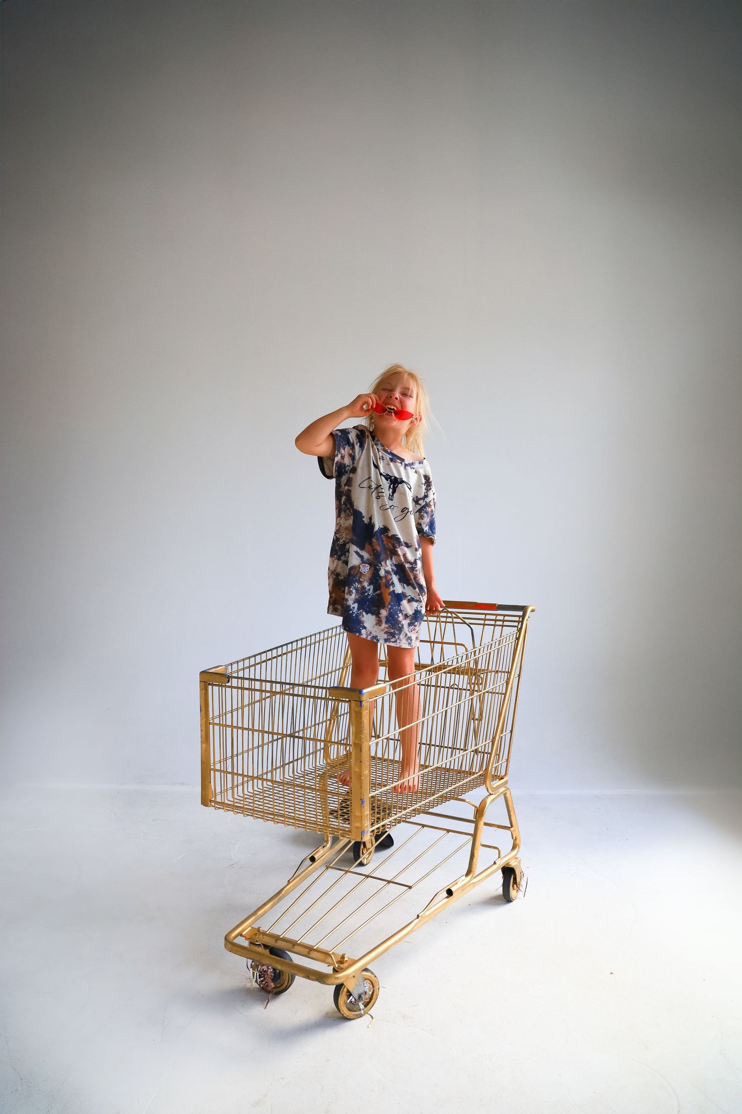 Creative fashion shot of person standing on gold shopping cart against white studio backdrop.