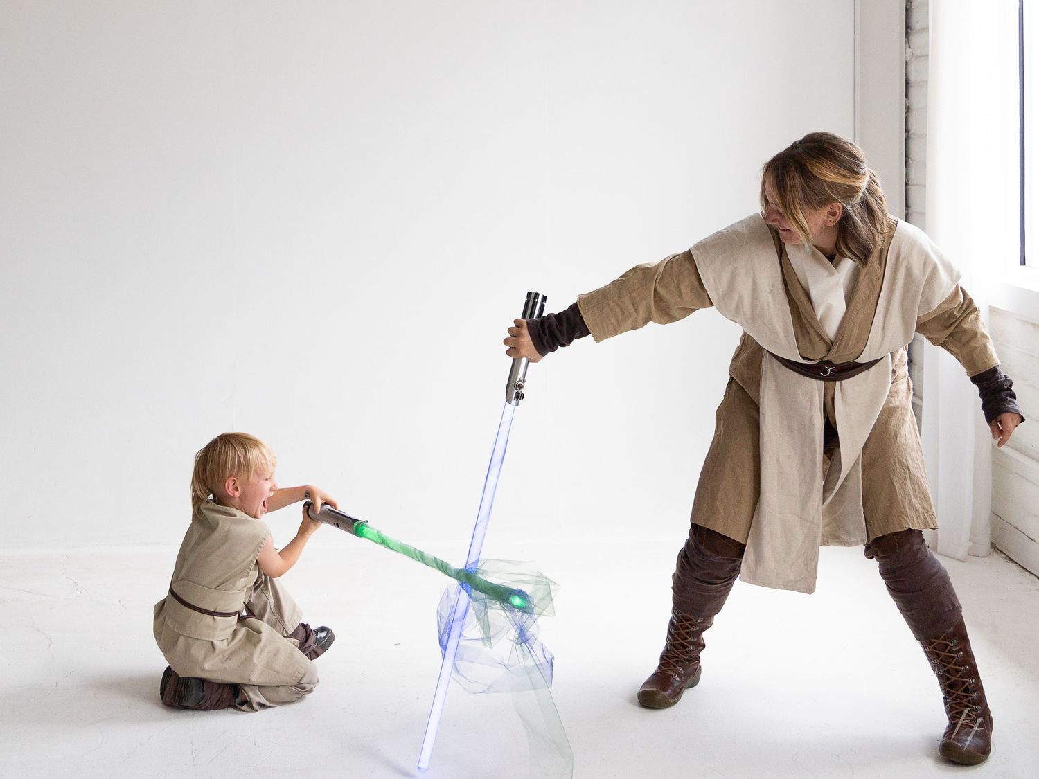 Two people dressed in Star Wars costumes engage in a lightsaber duel against a white background.