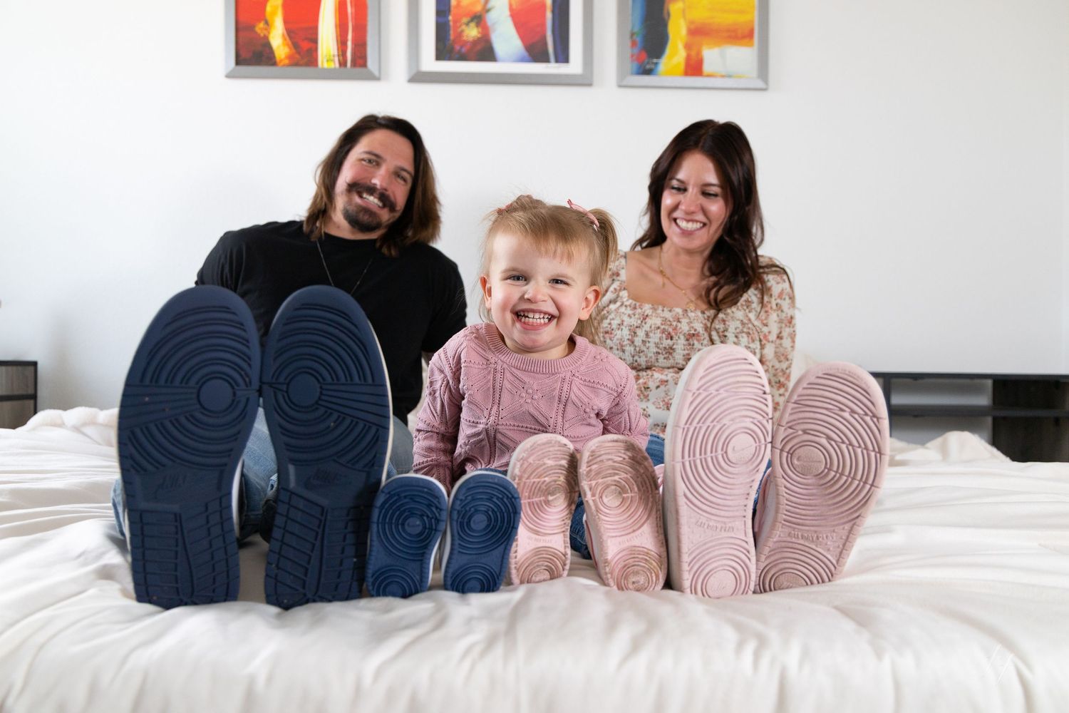 Family members wearing matching pink and navy pajamas lay together on a white bed showing off their cozy slipper socks.