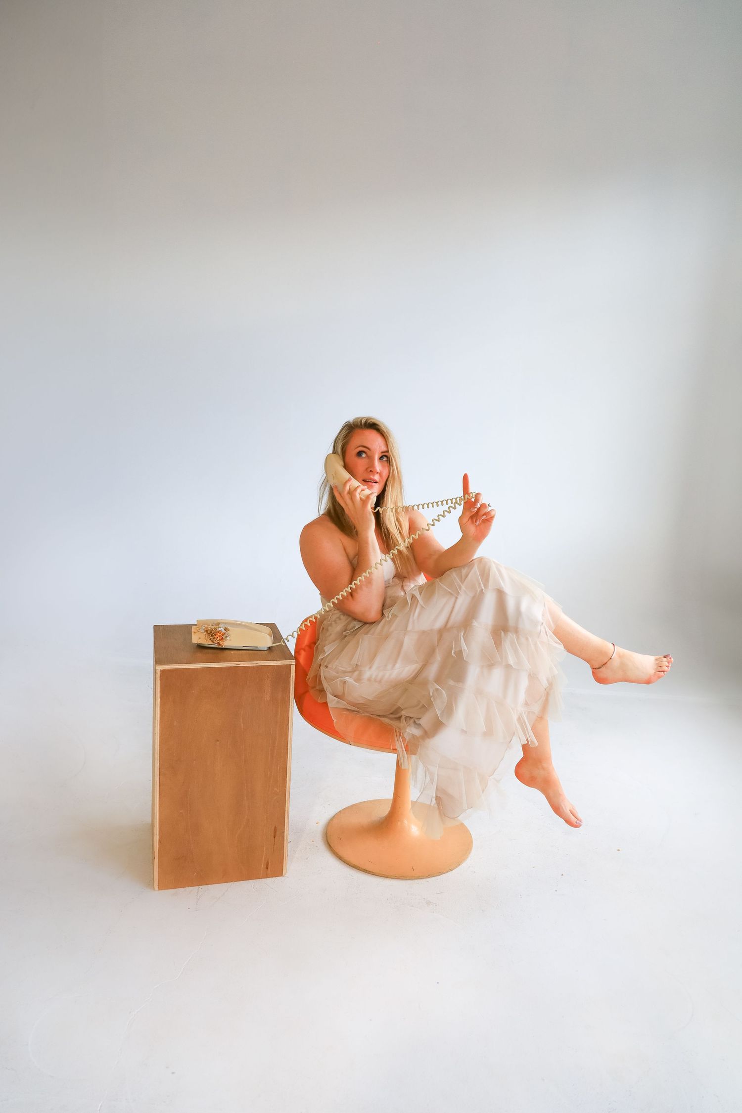 A figure in a flowing white dress performs expressive dance movements against a light gray studio backdrop.