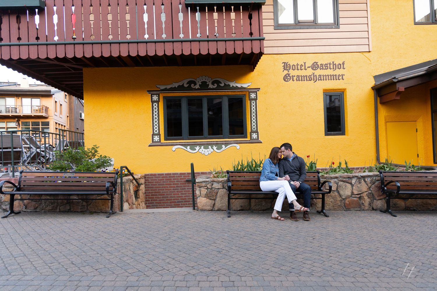 Couple sharing a romantic moment on a bench outside Hotel-Gasthof Gramshammer, a yellow Alpine-style building.