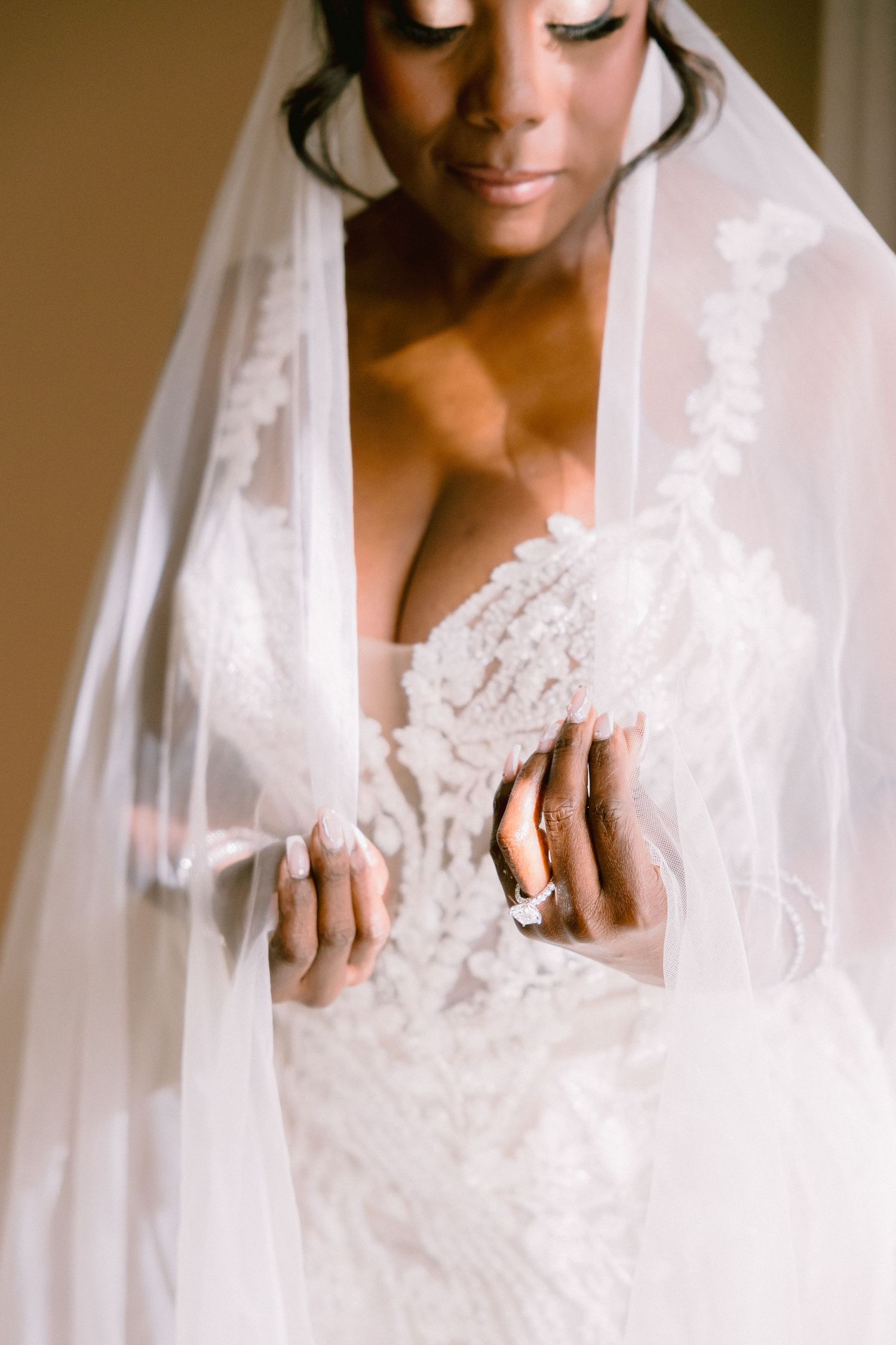 A bride in a white lace wedding dress and veil poses in soft natural light showing delicate details of her gown.