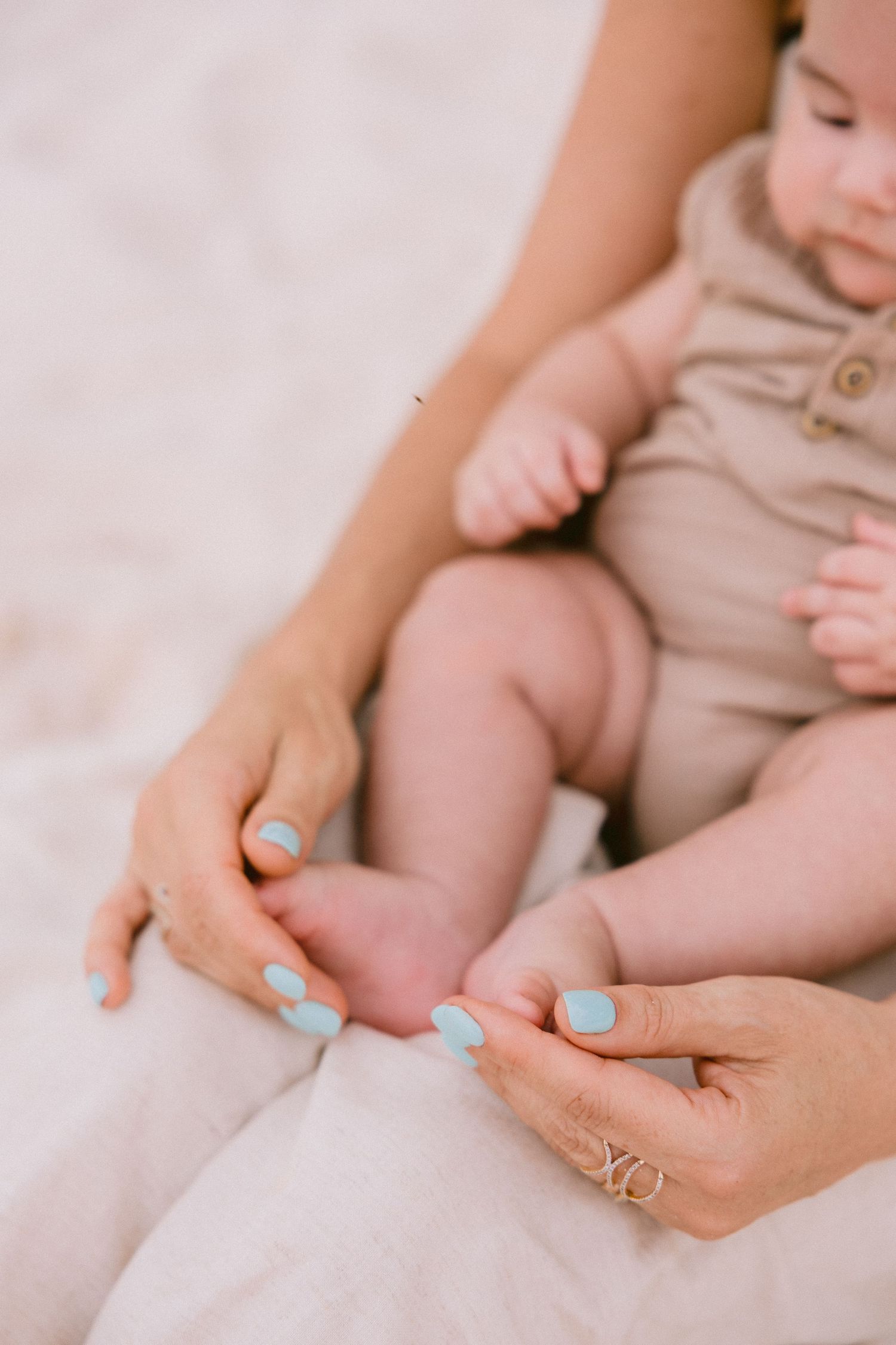 Close-up of hands with blue nail polish holding small baby feet.