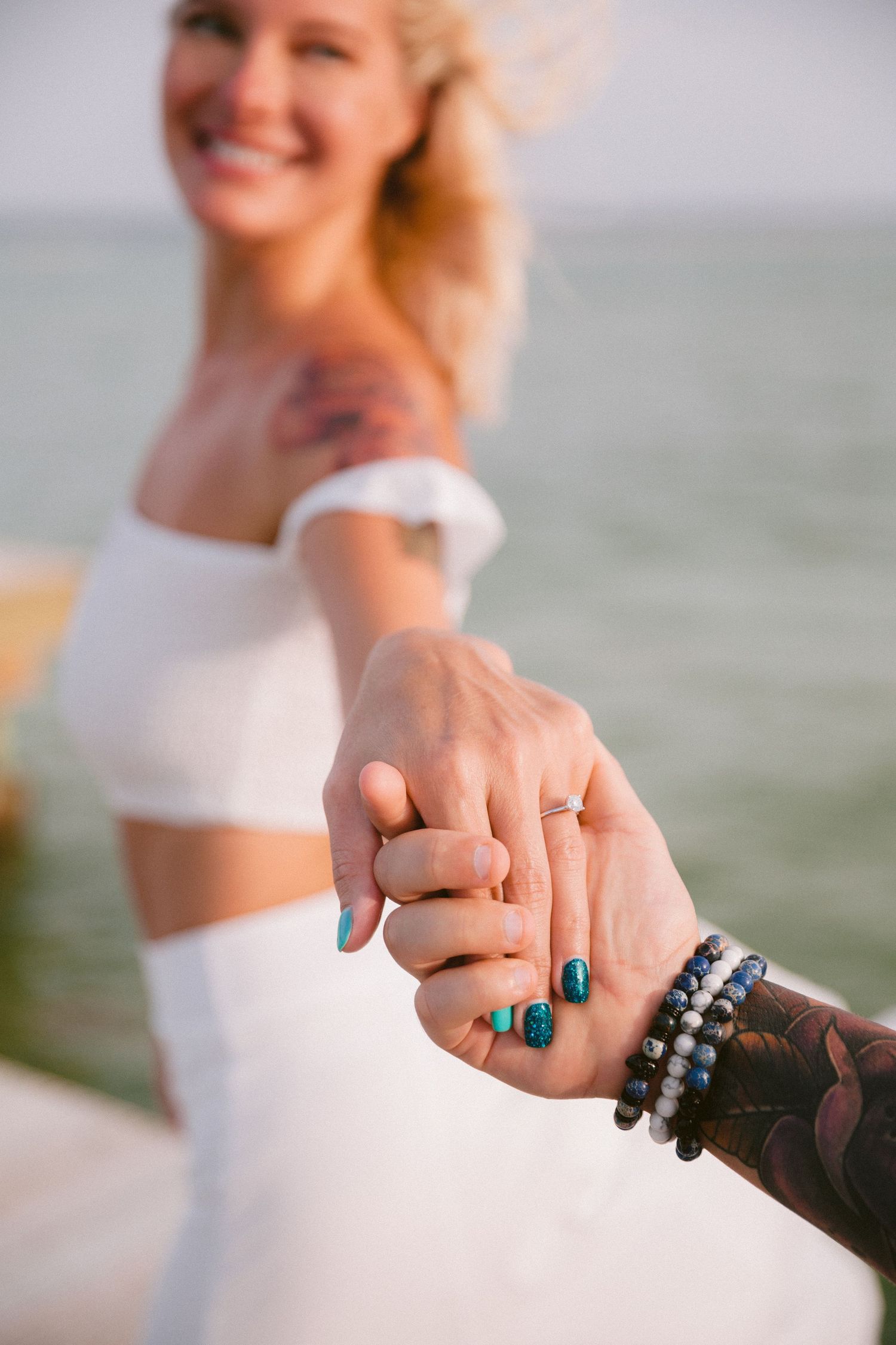 Close-up of hands with turquoise rings against an ocean backdrop.