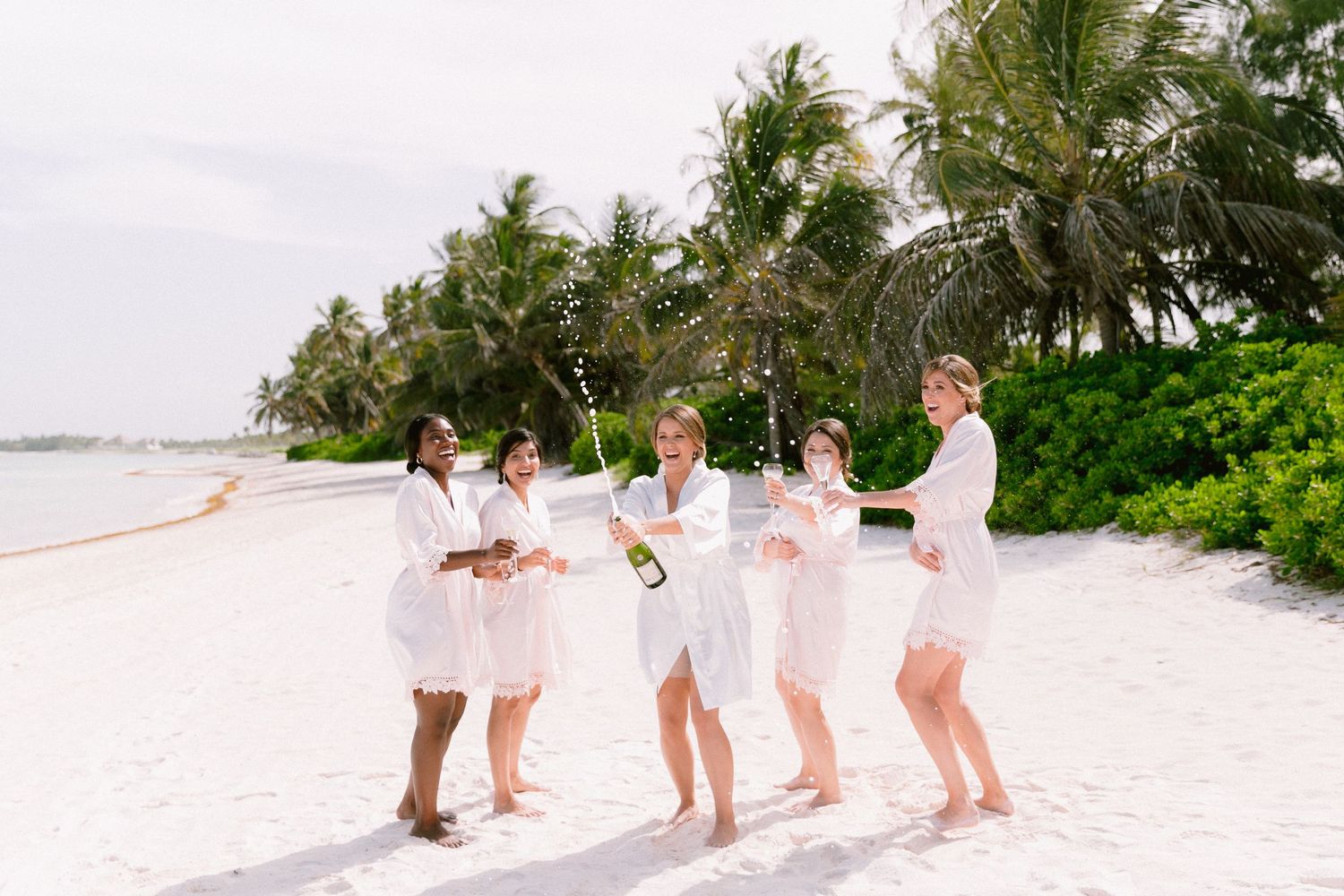 Group celebration on a tropical beach with matching white outfits.