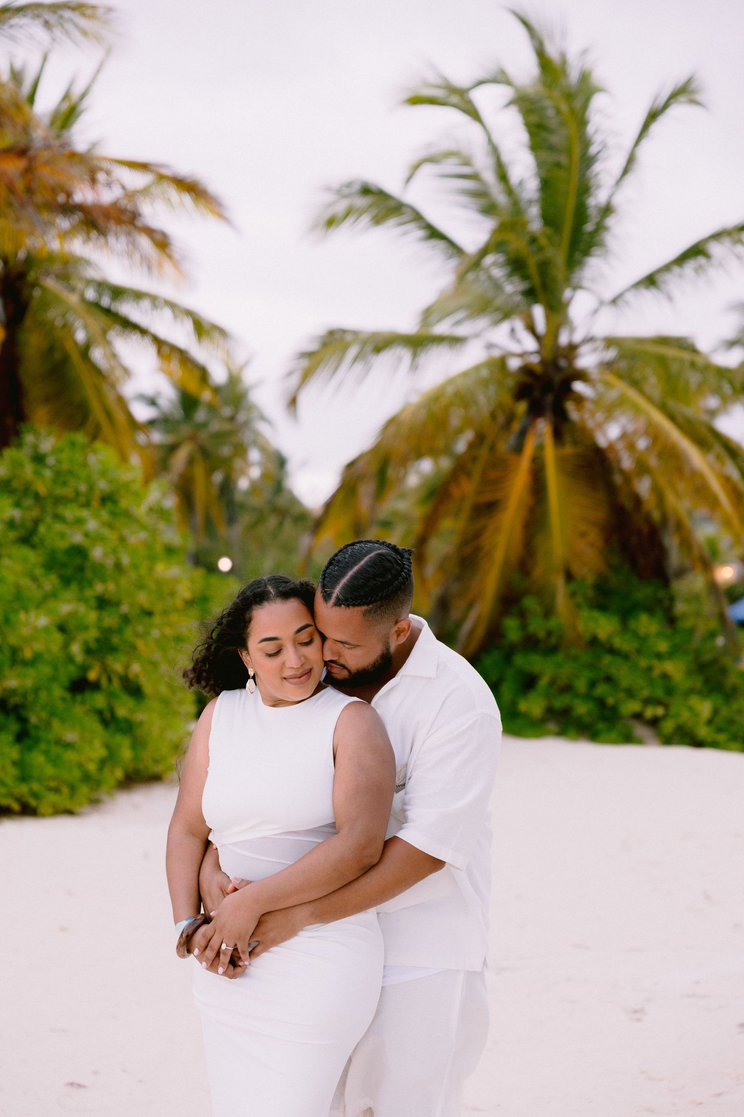 Romantic beach photoshoot with palm trees swaying in background.