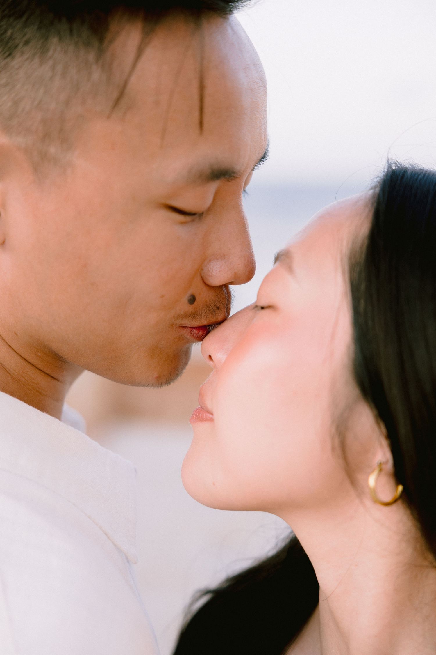 Close-up of an Asian couple sharing a tender kiss outdoors, with soft natural lighting creating a romantic atmosphere.