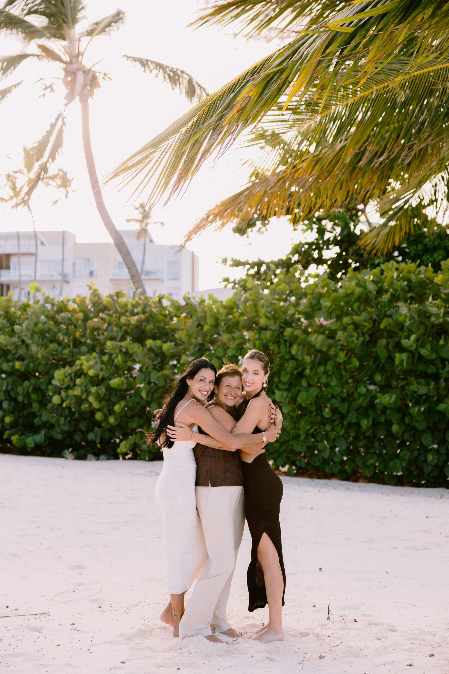 Three people embrace on a tropical beach during golden hour.